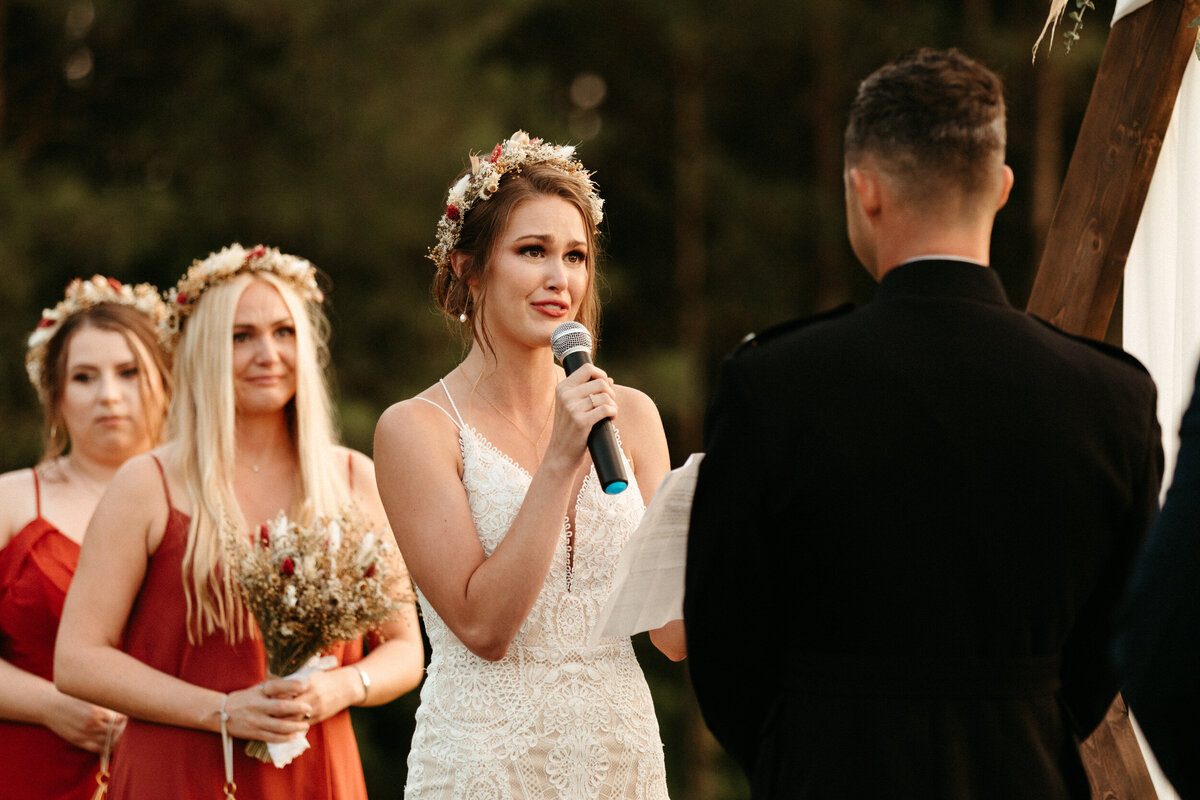 Emotional boho bride wearing flower crown and reading her vows to her groom at the alter during their wedding ceremony