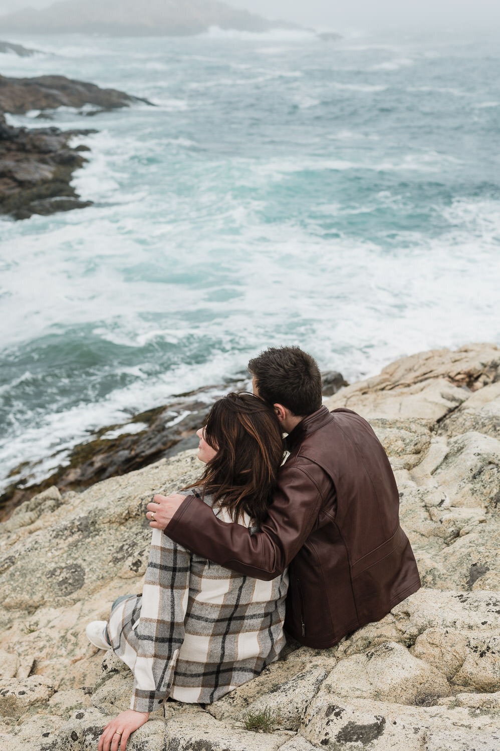 Couple sitting on the rocks, looking out to rough waters.