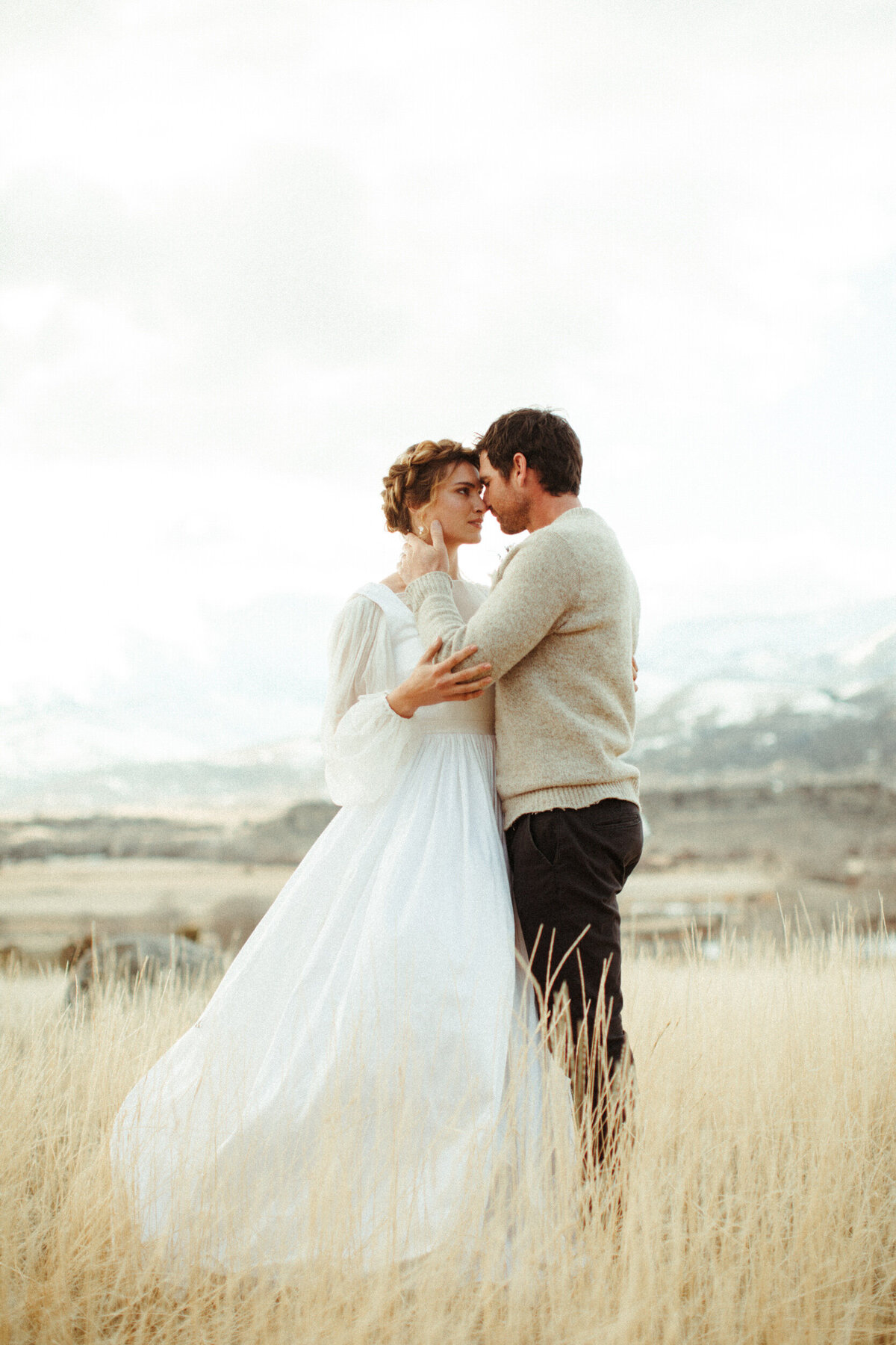 Boho bride with braided updo embracing her groom in a field during their winter elopement