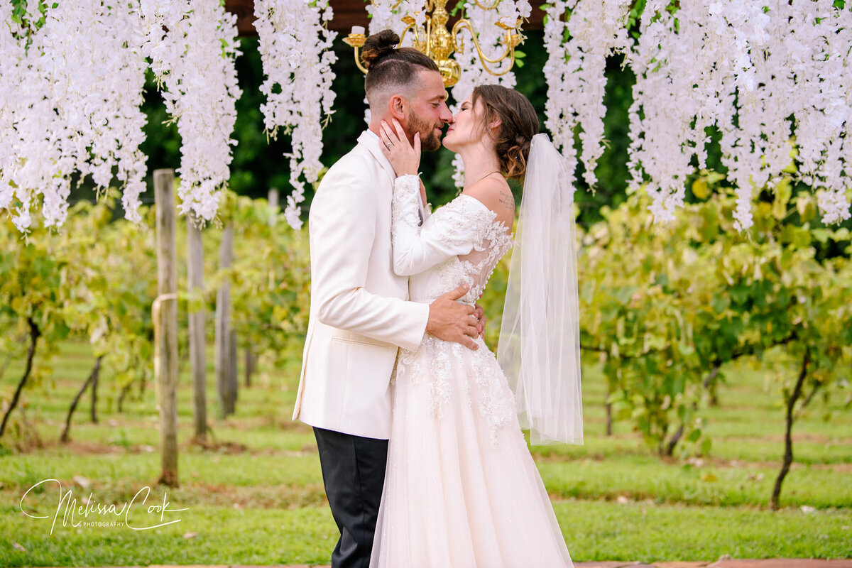 Bride and Groom Kiss with northern VA vineyard and flowers in background