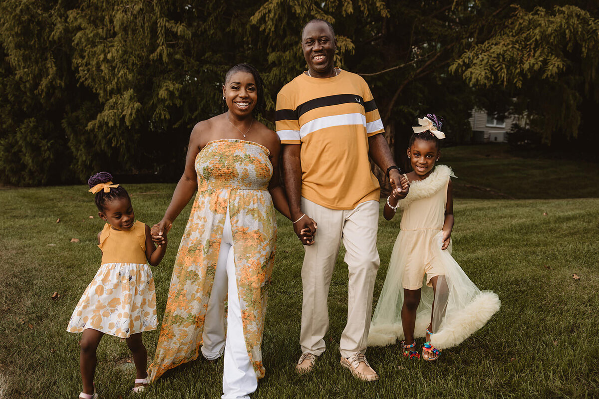 Parents holding their kids hands as they all walk in a field 