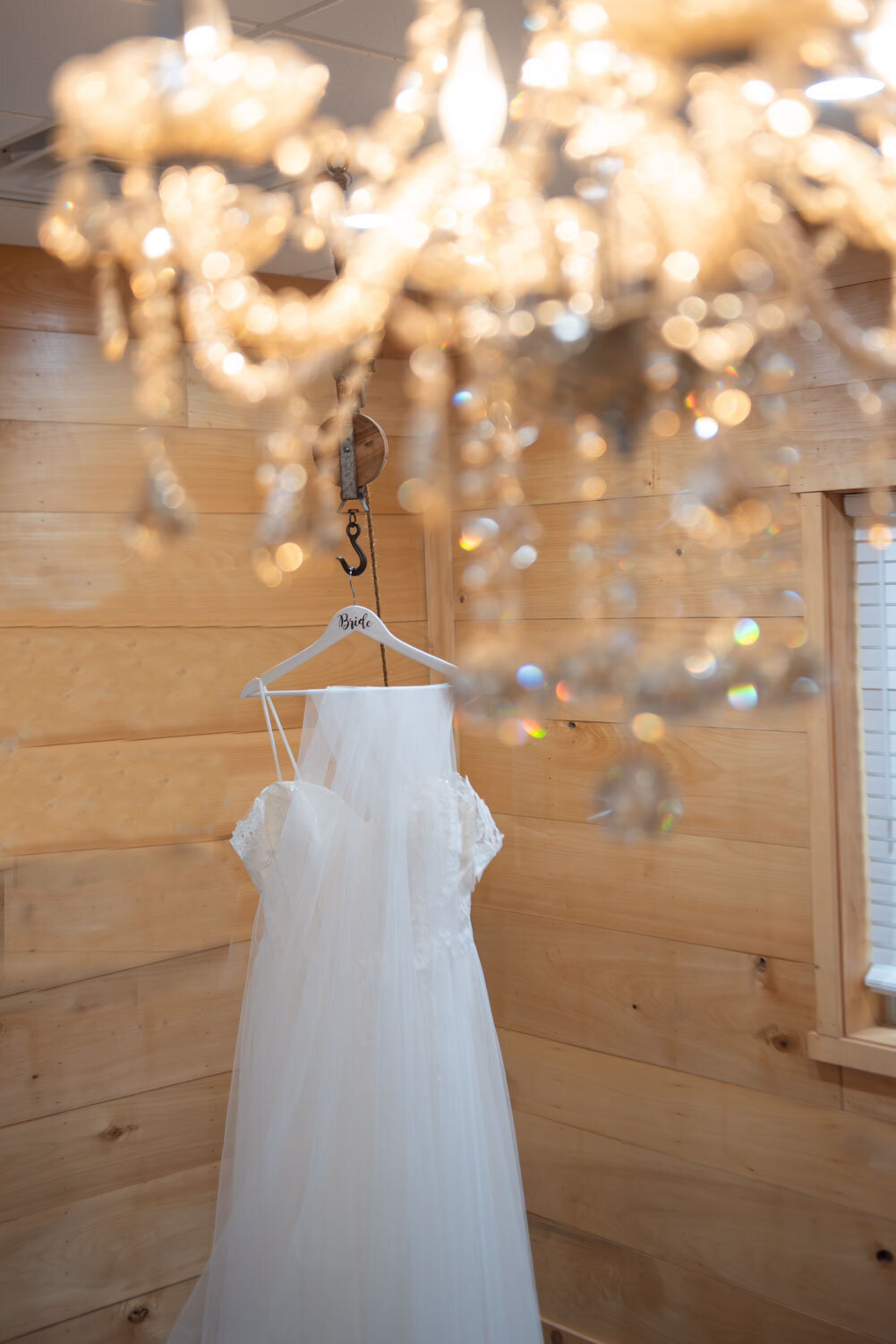 Wedding dress hanging in a rustic room with chandelier reflections