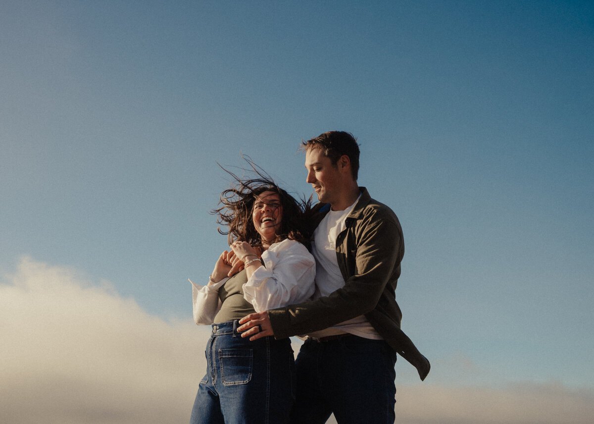 joyful couple laughing together near the shoreline during an engagement session on the Oregon coast