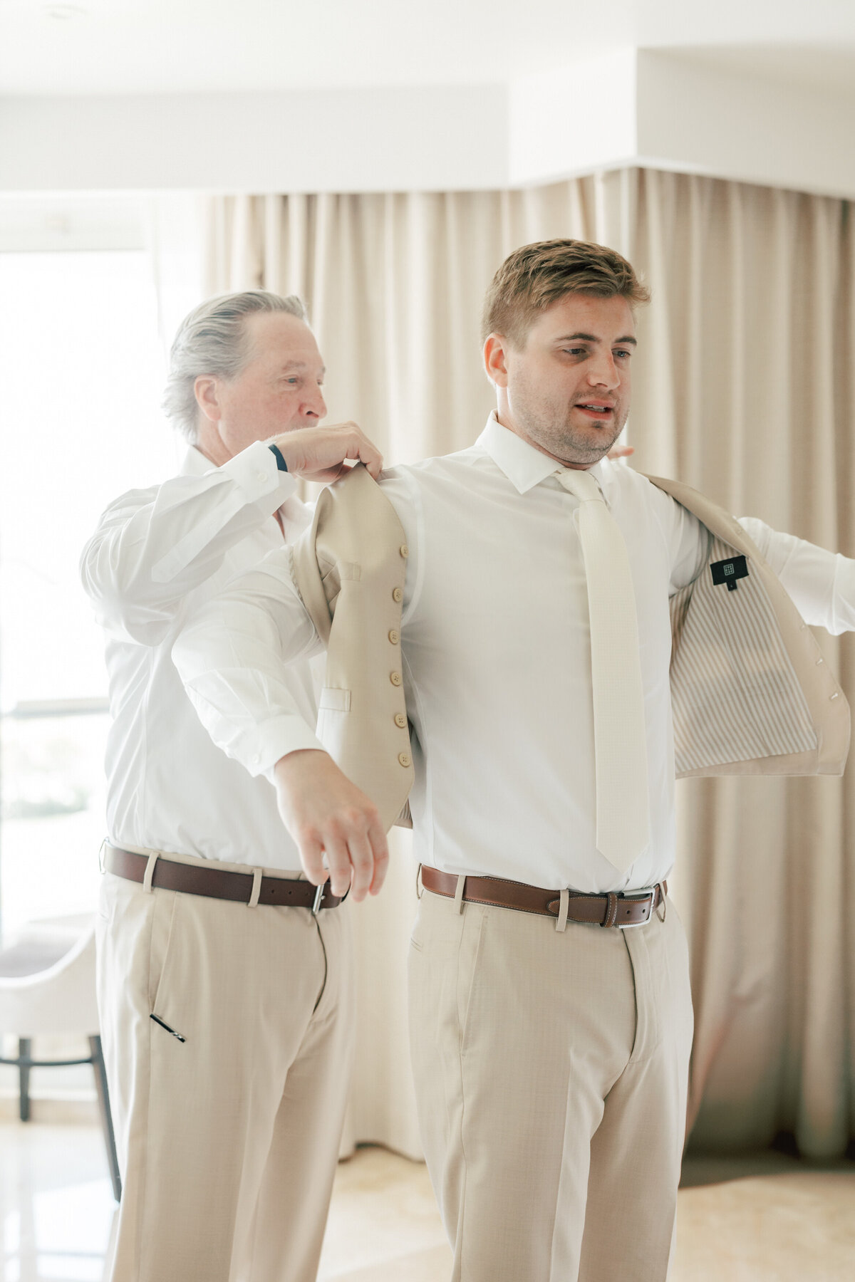 Groom getting help with tan suit jacket in Cancun, Mexico, by Philadelphia-based wedding photographer.