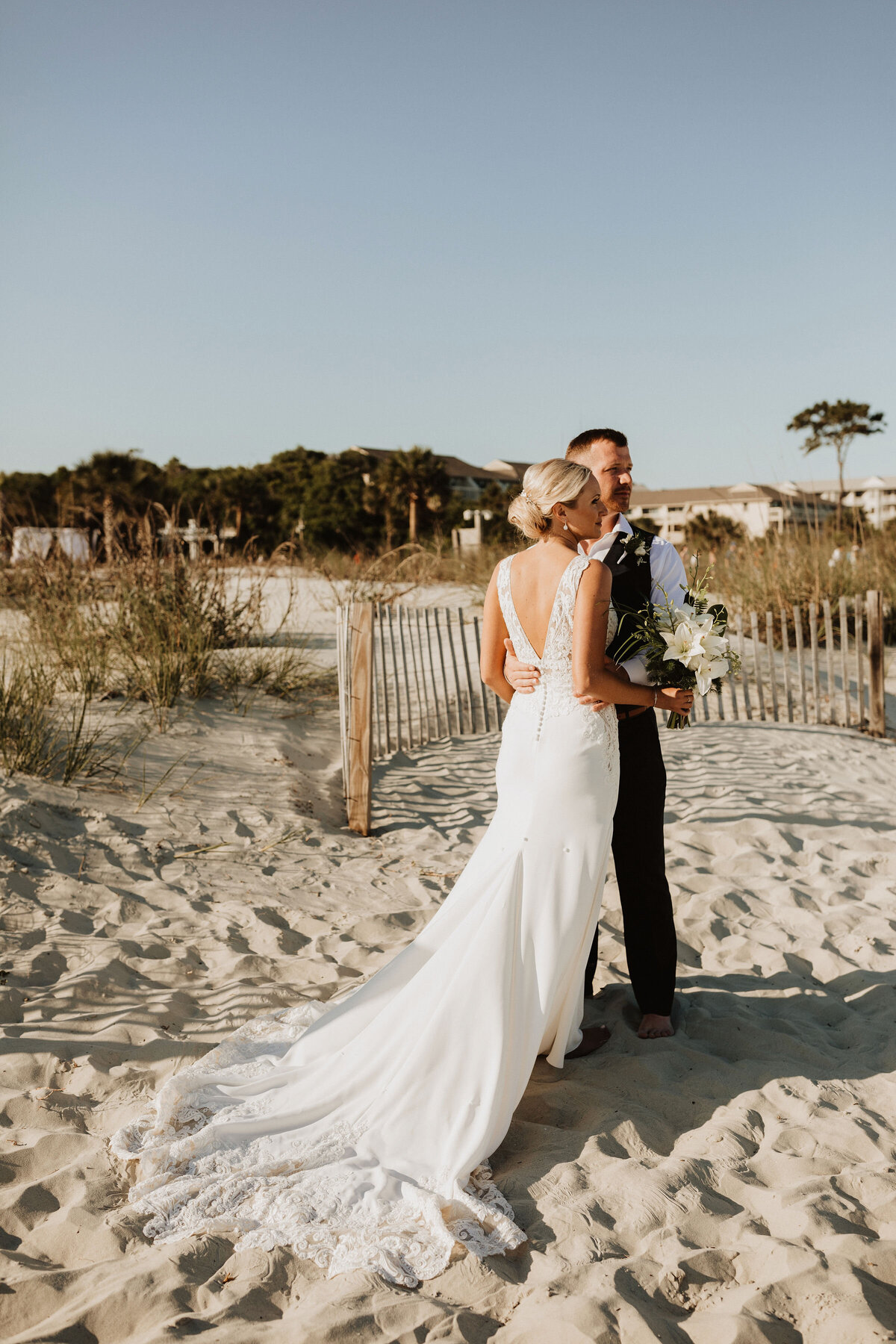 bride and groom stand on a white sand beach