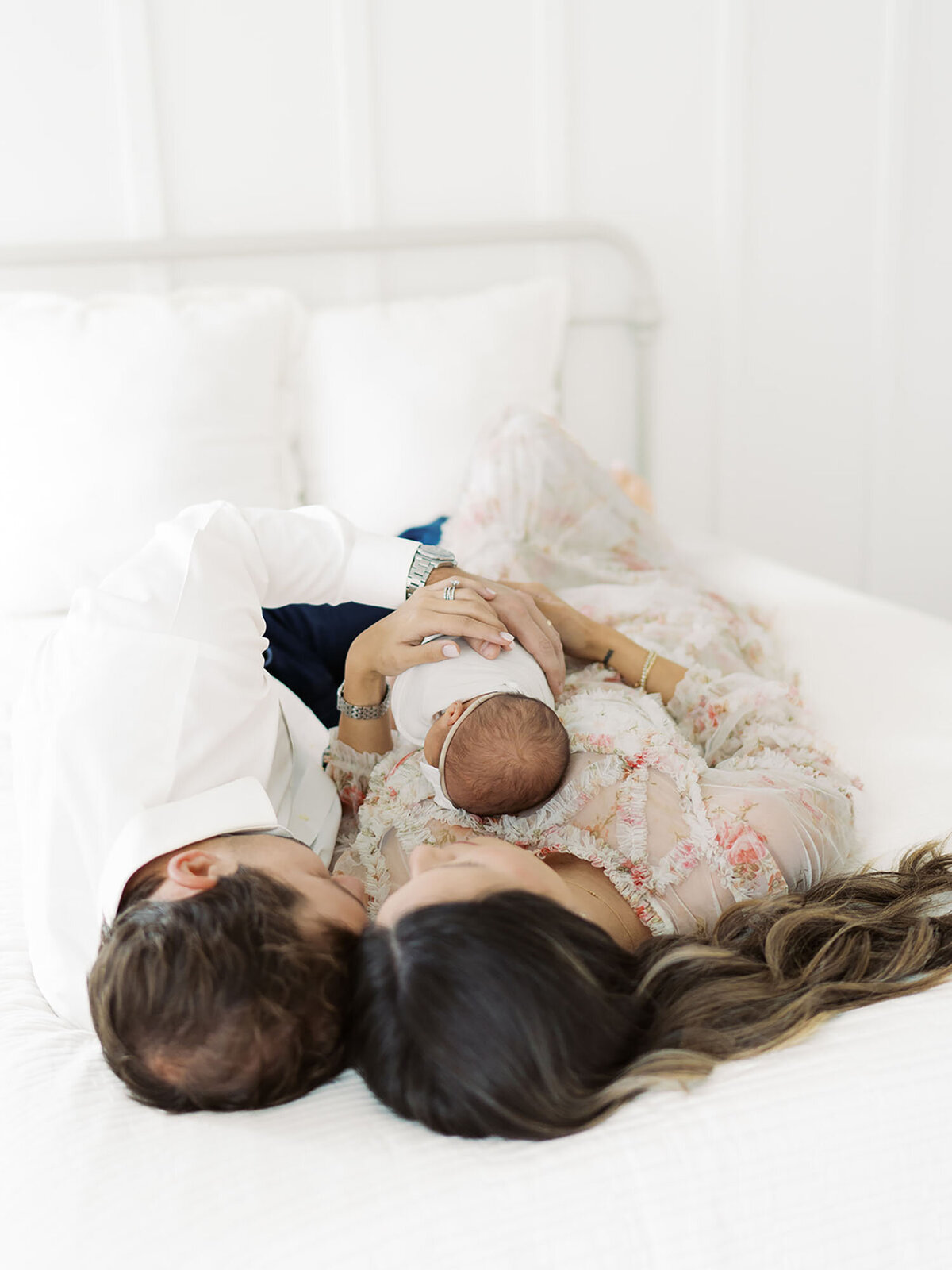 A mother and father lying on their bed, gently holding their newborn baby during a cozy in-home lifestyle newborn session, captured by Austin Newborn Photographer Teressa Jane