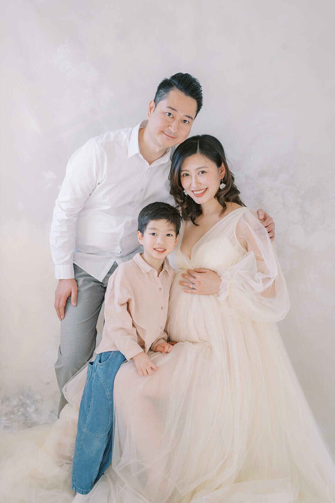 Anticipating joy, an Asian Chinese family illuminates a Gold Coast maternity photography studio in a dreamy cream tulle gown.