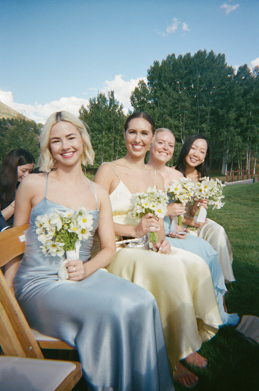 Seated bridesmaids smile and hold their elegant white bouquets amid the beautiful scenery at the Aspen Meadows Resort wedding ceremony.