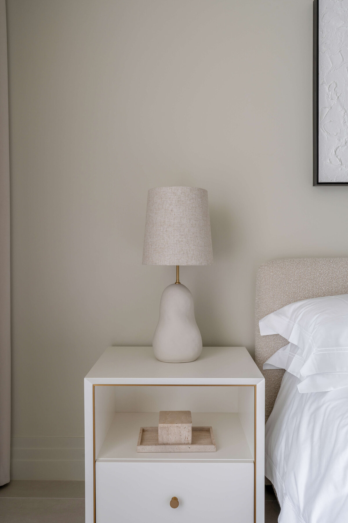 Sleek white side table with a neutral lamp next to a white bed in a light and airy guest bedroom.