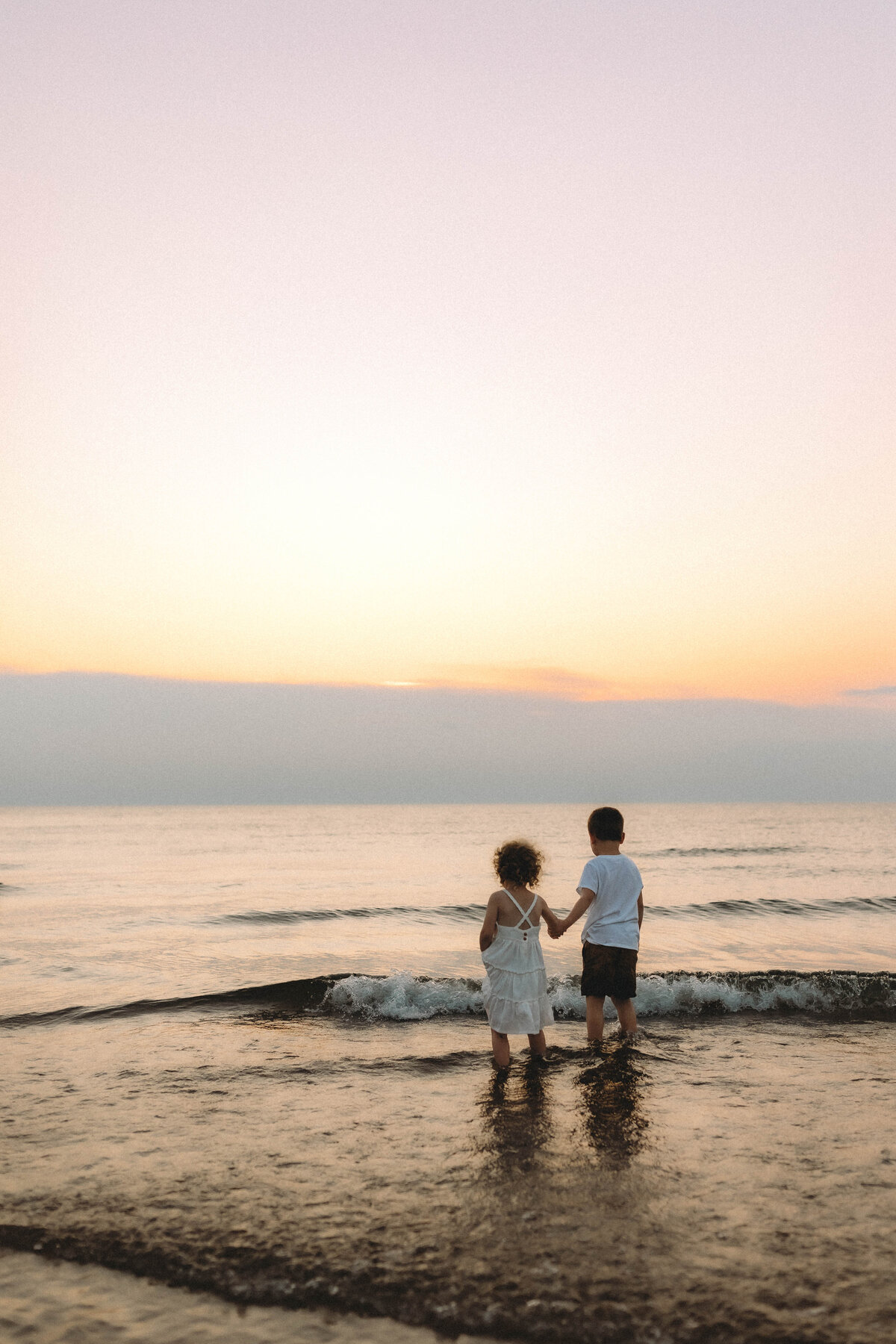 children hold hands and watch the sunset at new buffalo beach 