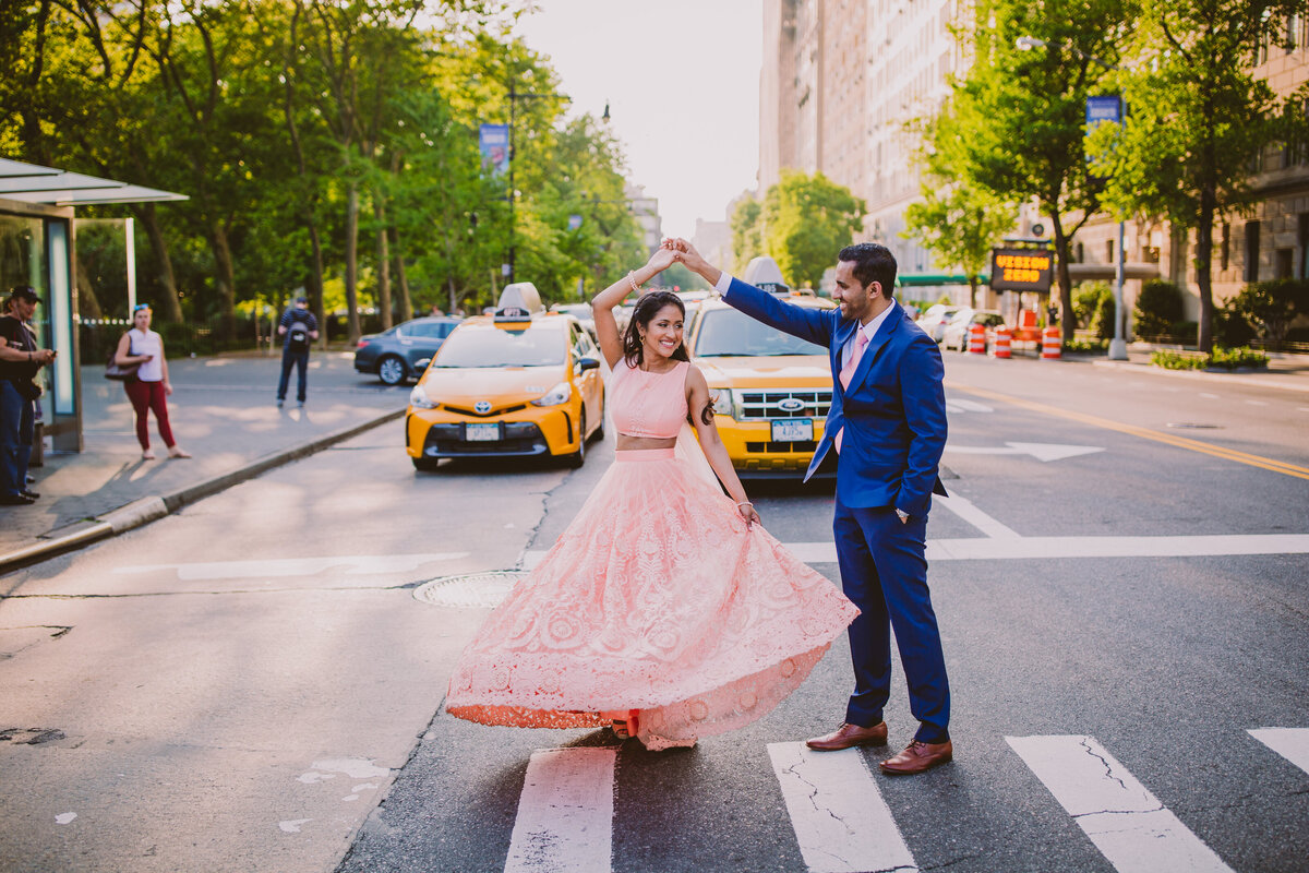 An engaged couple in indian clothing twirl in the middle of the crosswalk in new york city