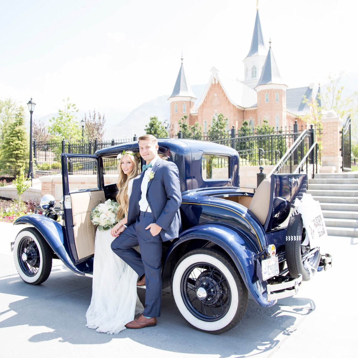 A gorgeous wedding couple posing in front of a vintage blue car by the provo city center lds temple