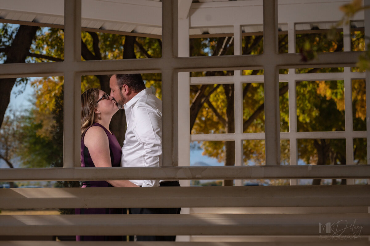 bride and groom kiss in the gazebo at golden hour  fall elopement to las vegas  Dry lake Bed elopement Blue Suit on Groom  flowers by michelle  bride in cream color wedding dress with deep  plunging  neckline mountain skyline  sunset las vegas wedding photographers mk delacy photography