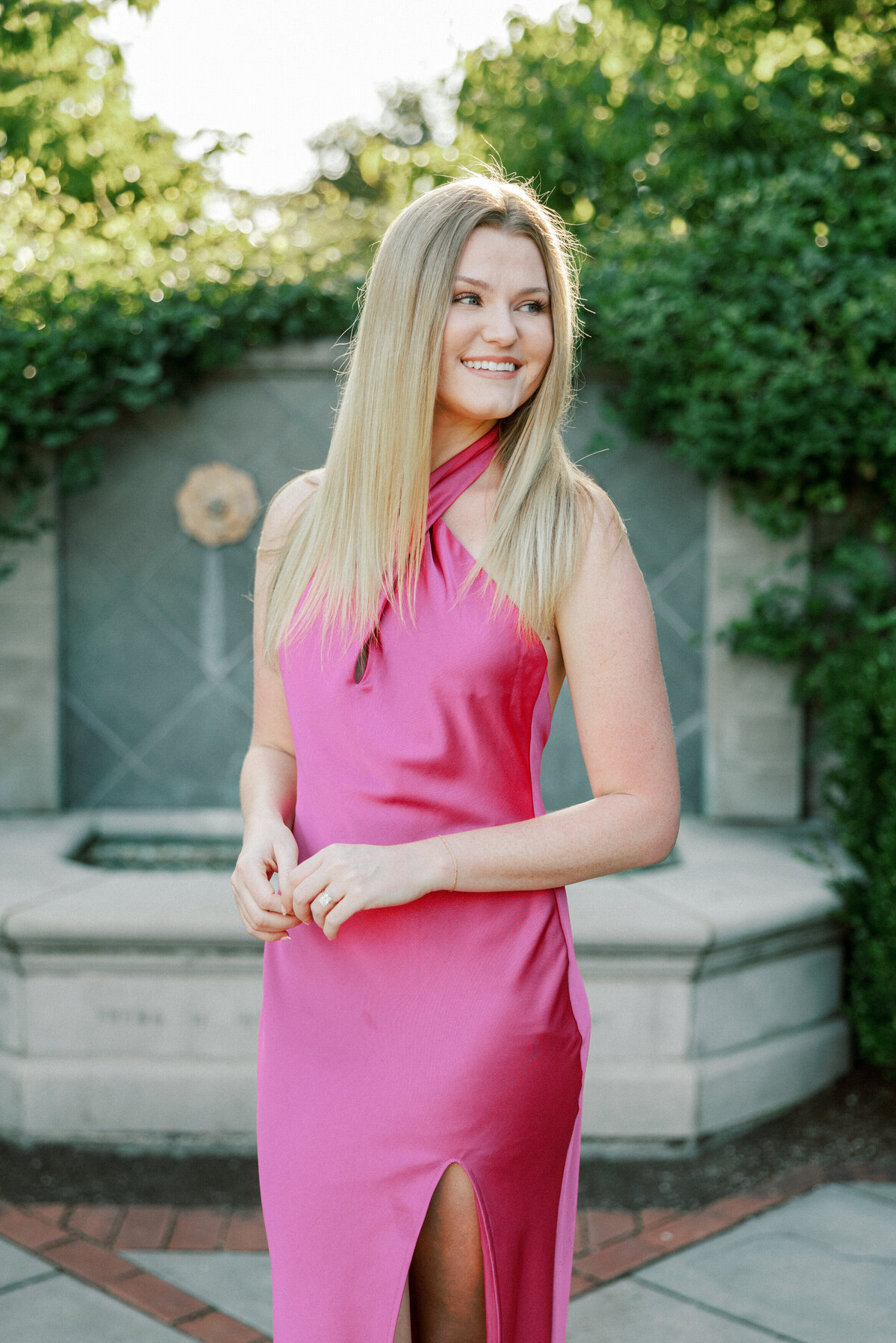 Woman in pink dress looking to her side poses in front of stone fountain in Columbus park.