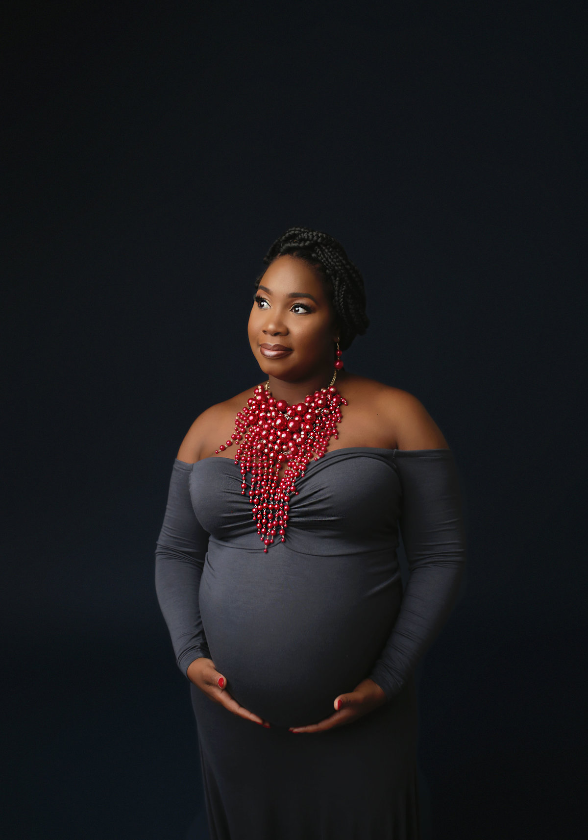 black pregnant mother holding belly in gray dress with bold red necklace