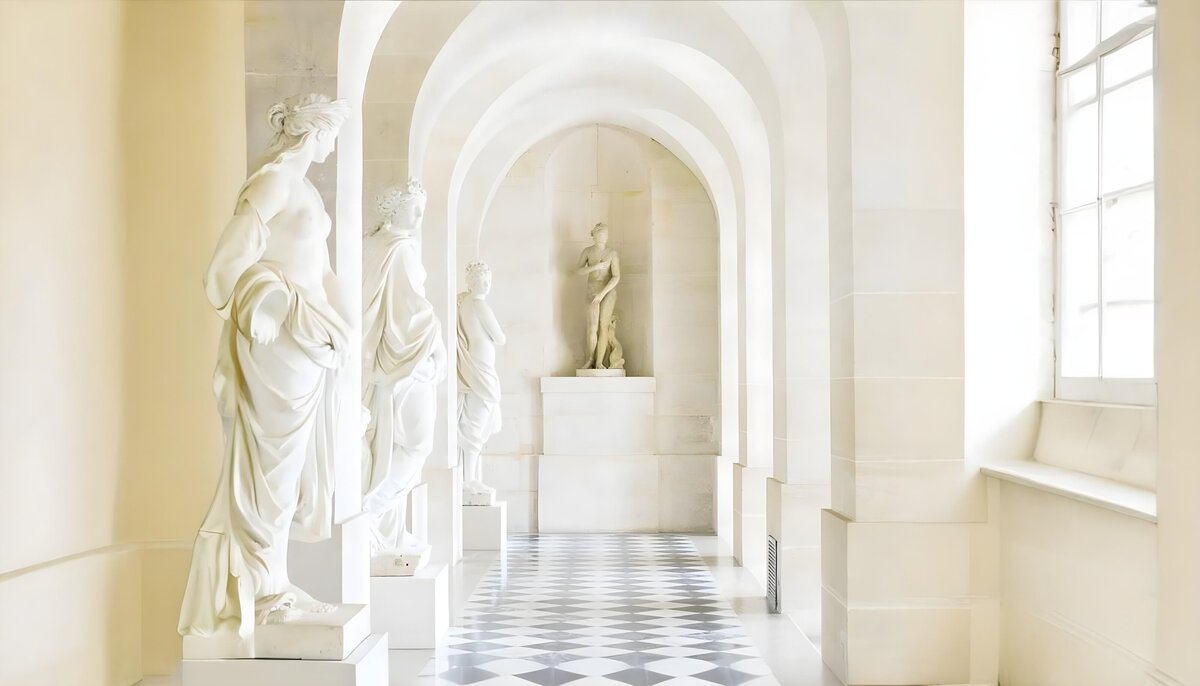 Alignement de statues blanches dans un couloir agrémenté d'arches et de carrelage à carreaux.