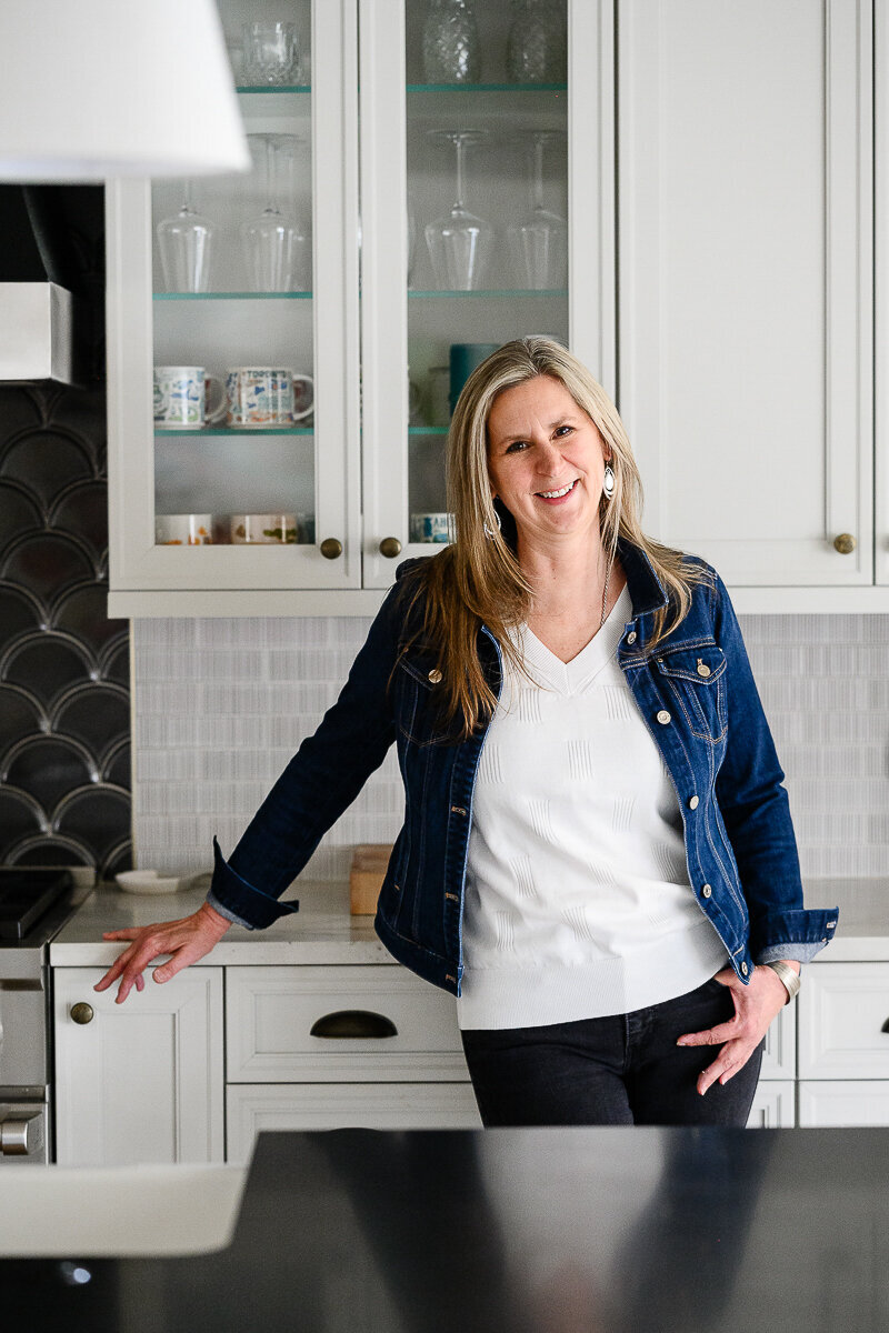 A brand photographer in Denver takes a photo of a woman leaning on a kitchen counter in her jean jacket for her brand pictures and brand photography session.