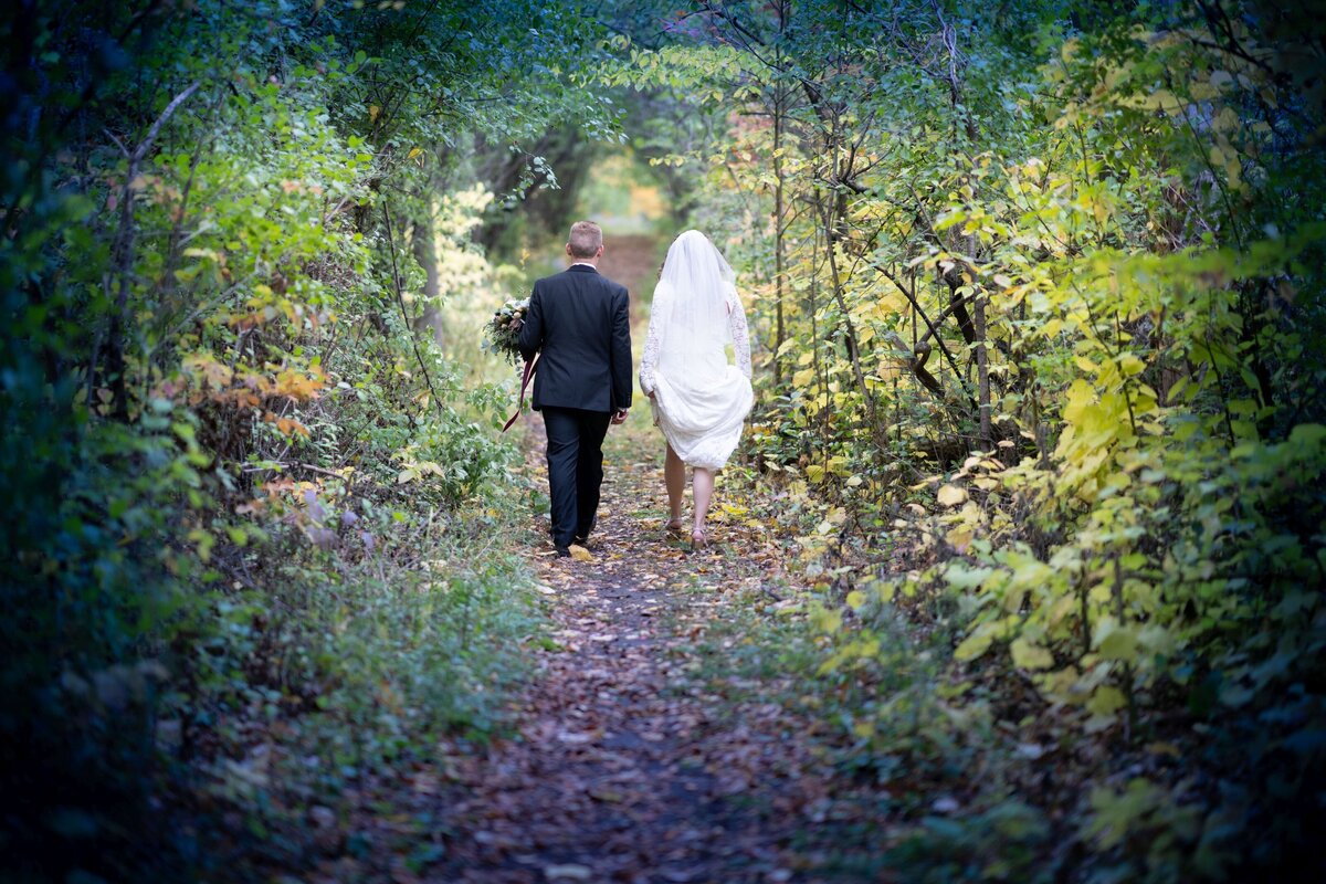 A romantic shot of a couple walking hand in hand through a serene forest path, surrounded by a natural tunnel of trees, creating an enchanting and intimate atmosphere.