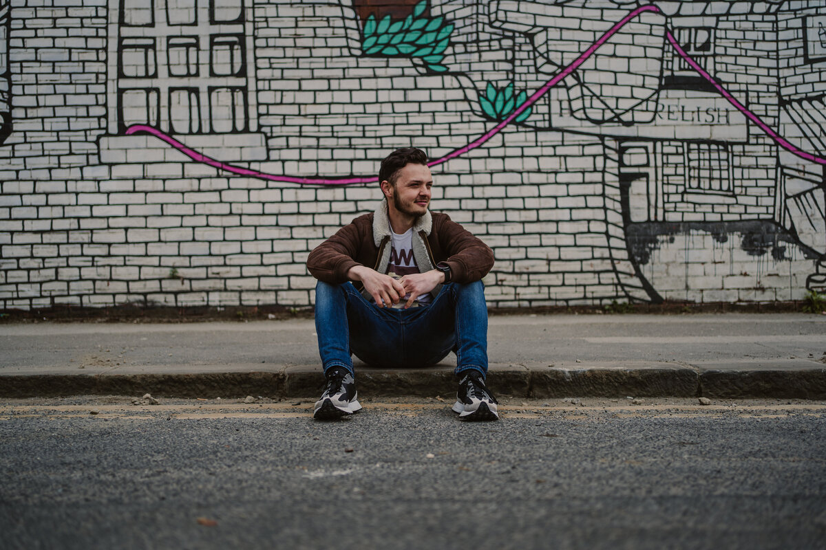 London wedding photographer sits  on a curb with cool street art as a backdrop
