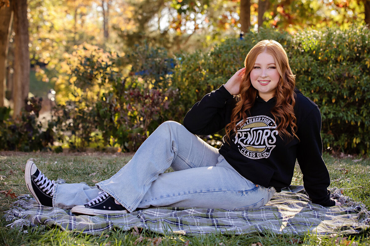 Portrait of a Cuthbertson HS senior wearing her SENIORS hoodie and jeans and sitting on a blanket during her senior portrait session
