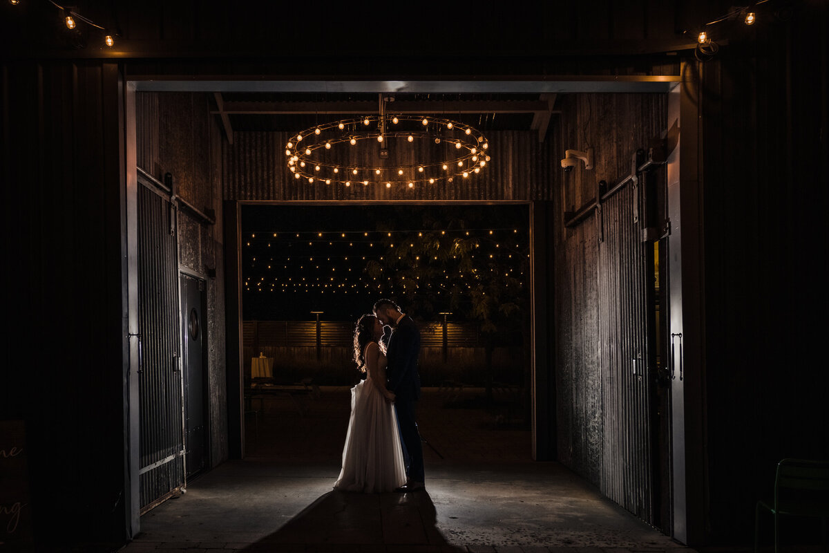 Bride and groom kiss with a light behind them outside at Warehouse109