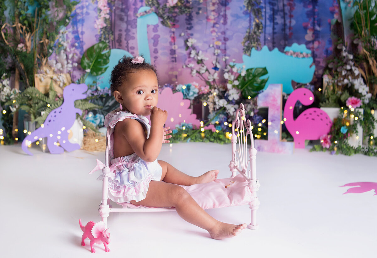 Baby girl sitting on little pink bed during cake smash photoshoot in Franklin Tennessee photography studio