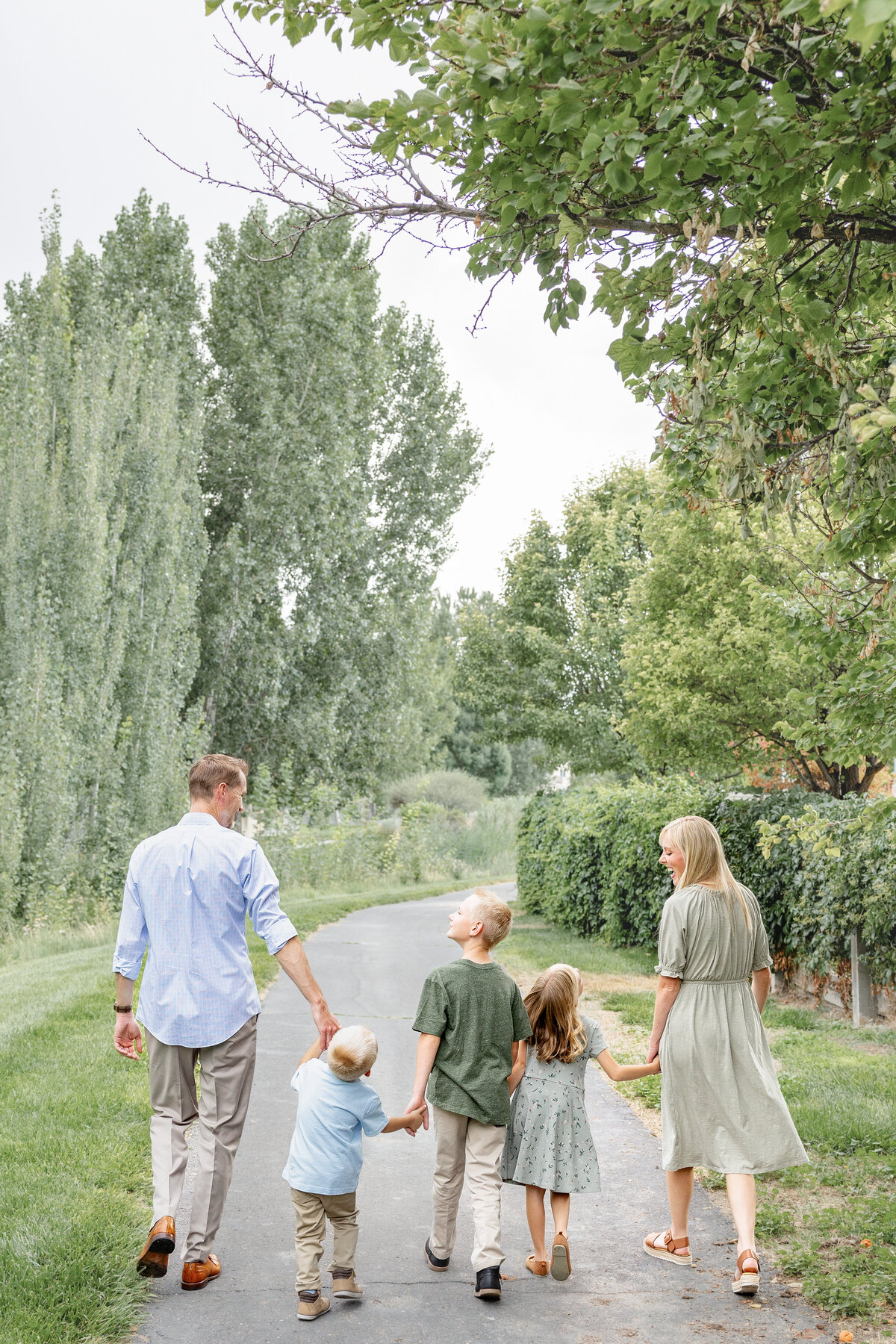A family of five walking down a scenic tree-lined path, holding hands and enjoying the peaceful outdoors in Eagle Mountain, Utah