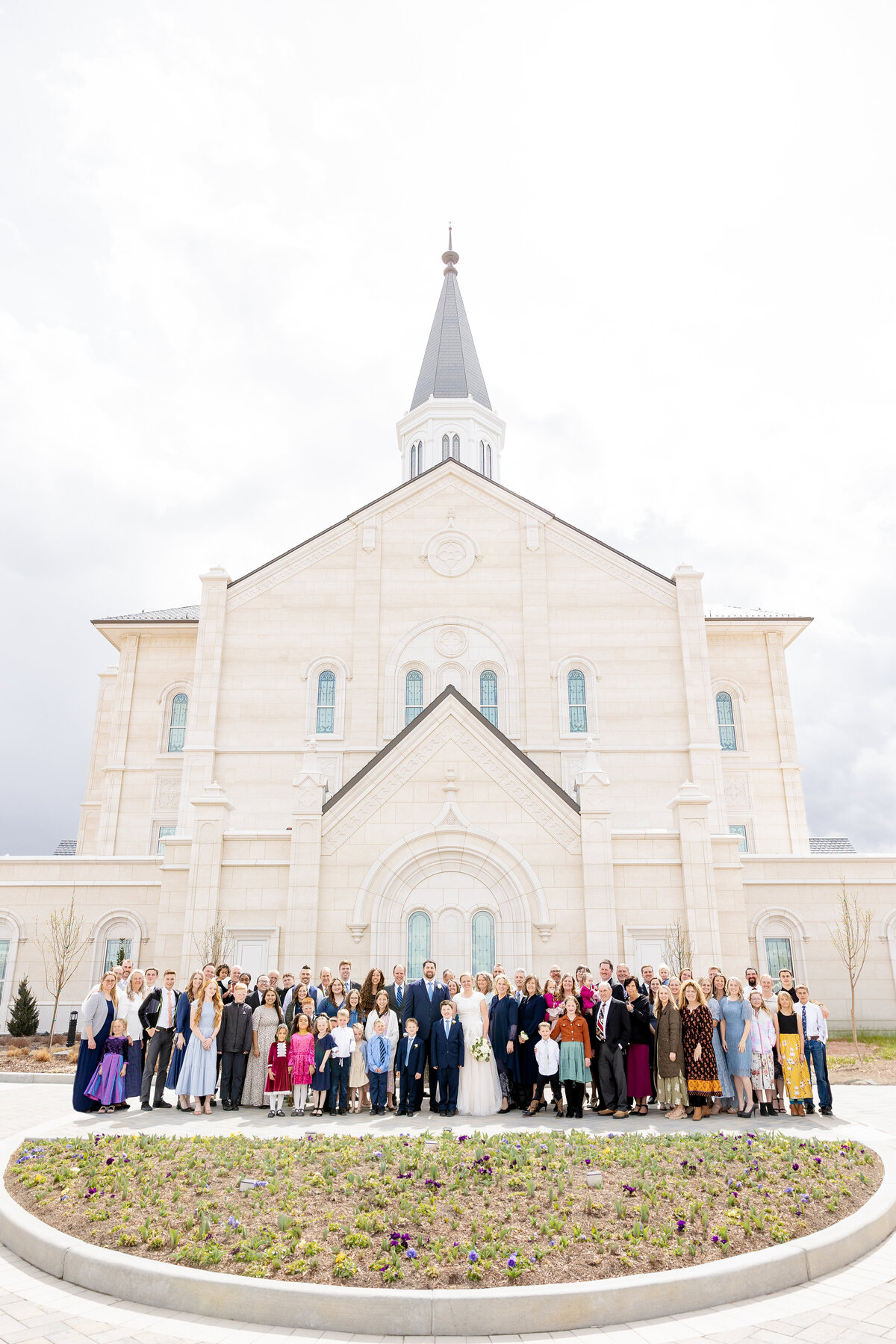  Large group photo of the bride, groom, and wedding guests standing in front of the Taylorsville Utah LDS Temple on a bright day.