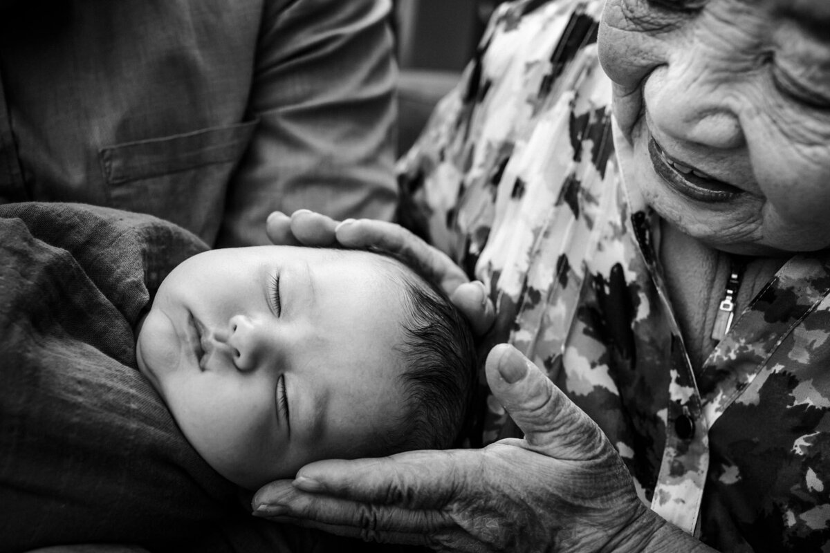 grandmother holding sleeping newborn's head while she looks down and smiles at him