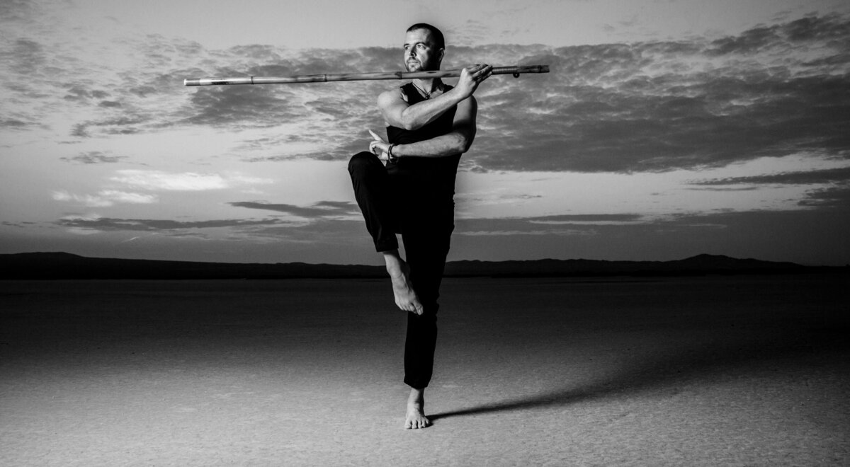 Black and white portrait musician Jason Campbell  in yoga pose middle of desert at sun rise El Mirage