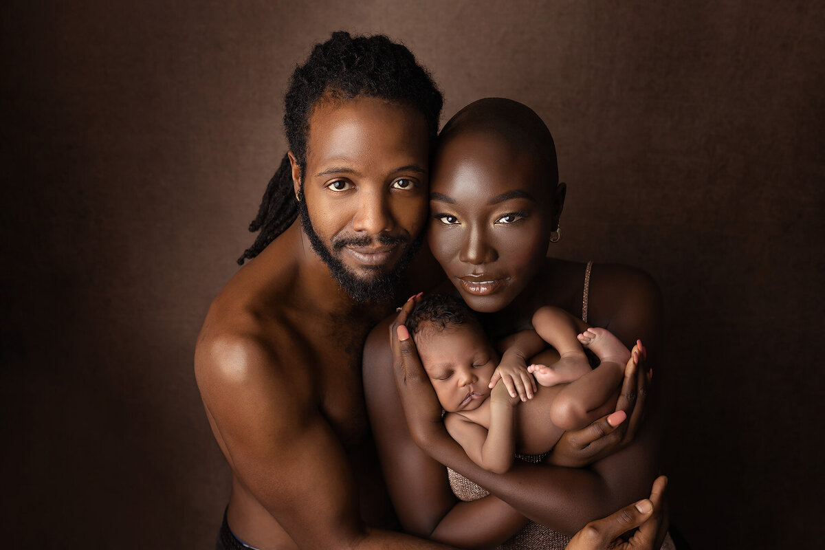Beautiful family holding their newborn baby against a rich brown backdrop captured by Dallas newborn photographer.