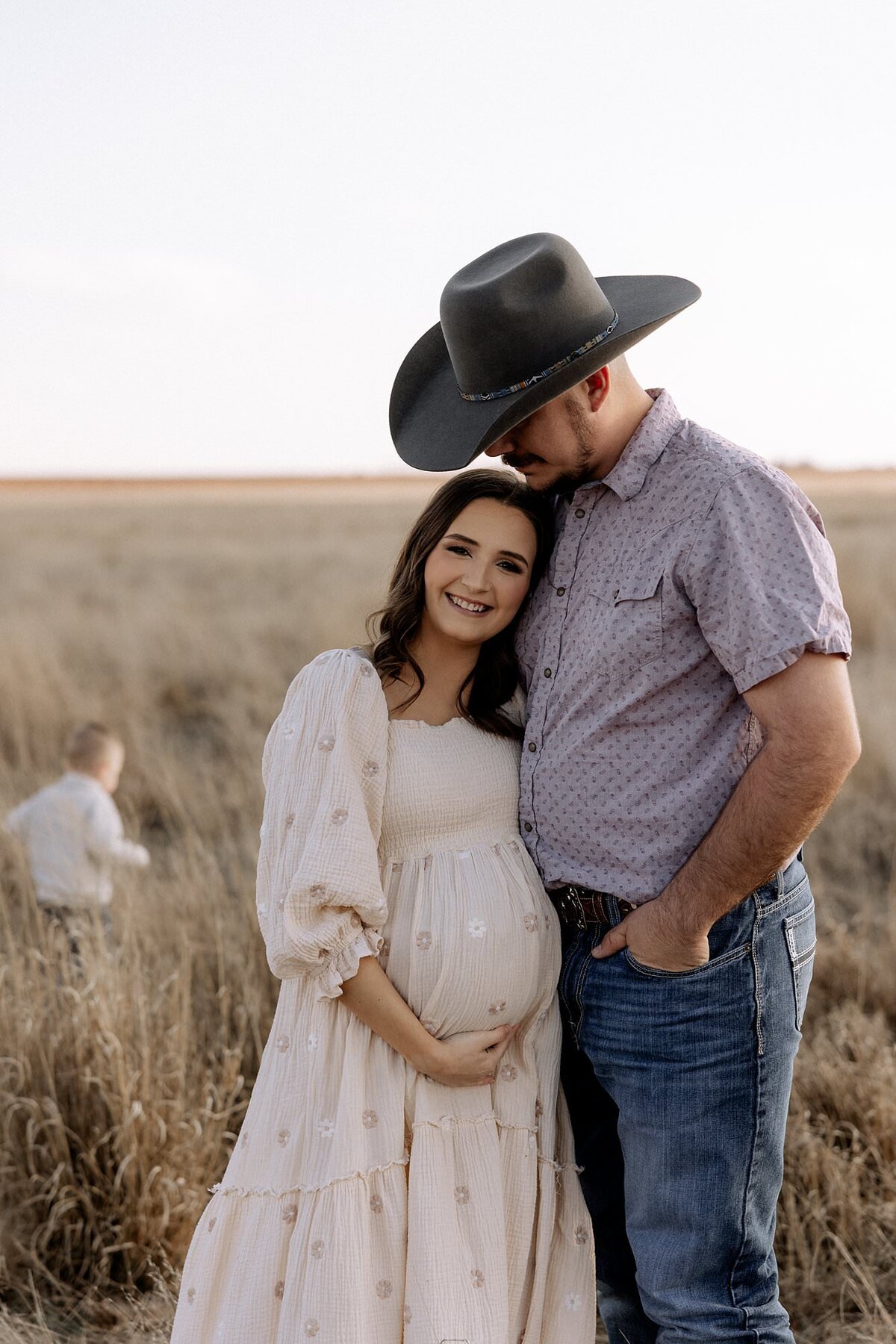 dad in cowboy hat arms wrapped around his pregnant with embracing