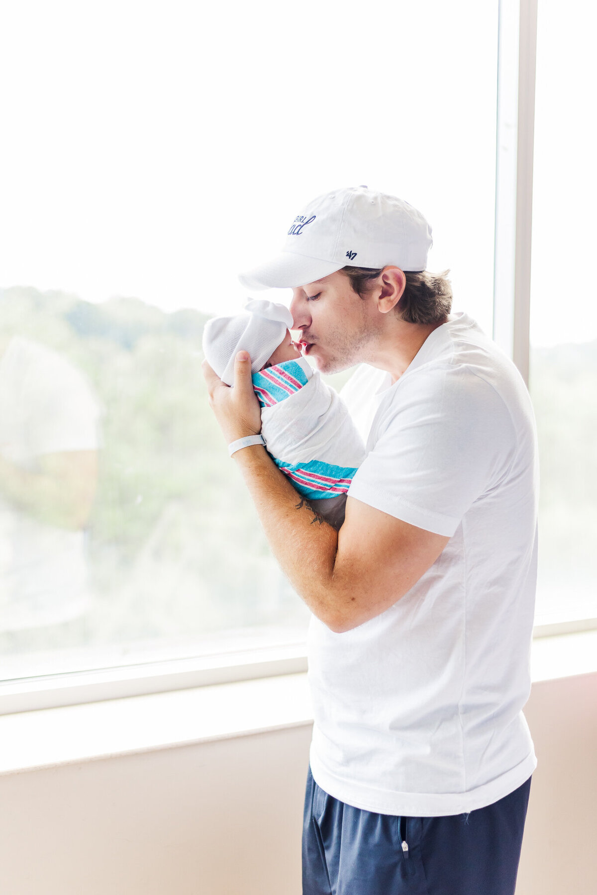 dad holding newborn baby girl wrapped in hospital blanket kissing her on the head