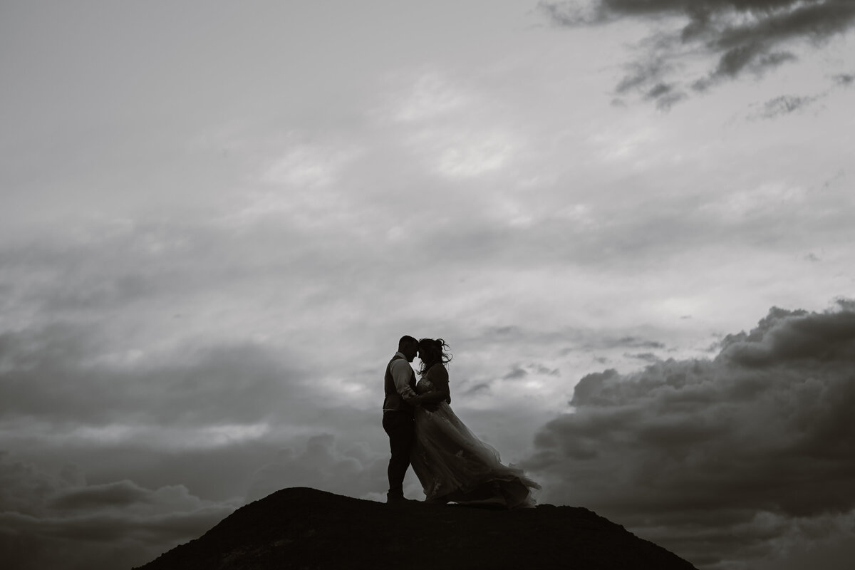 Black and white image of a couple kissing while standing at the top of a large rock