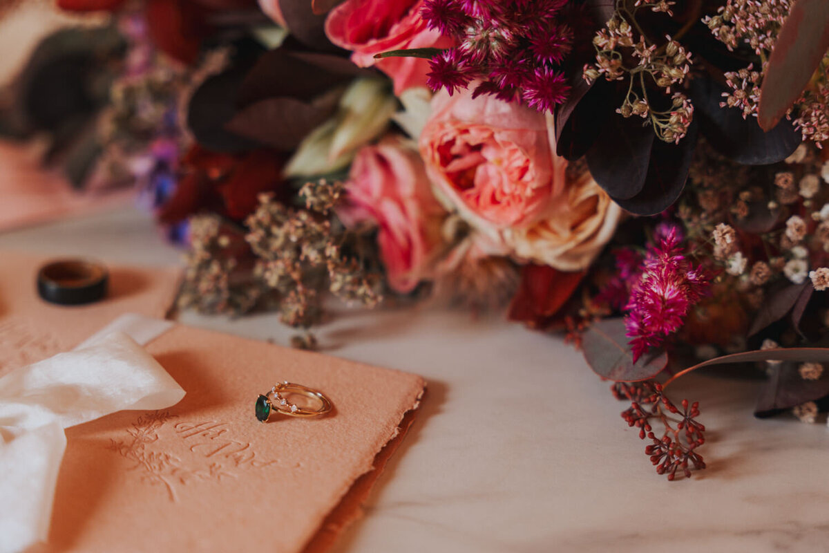 Pink, red, and purple wedding florals sit near wedding stationary 