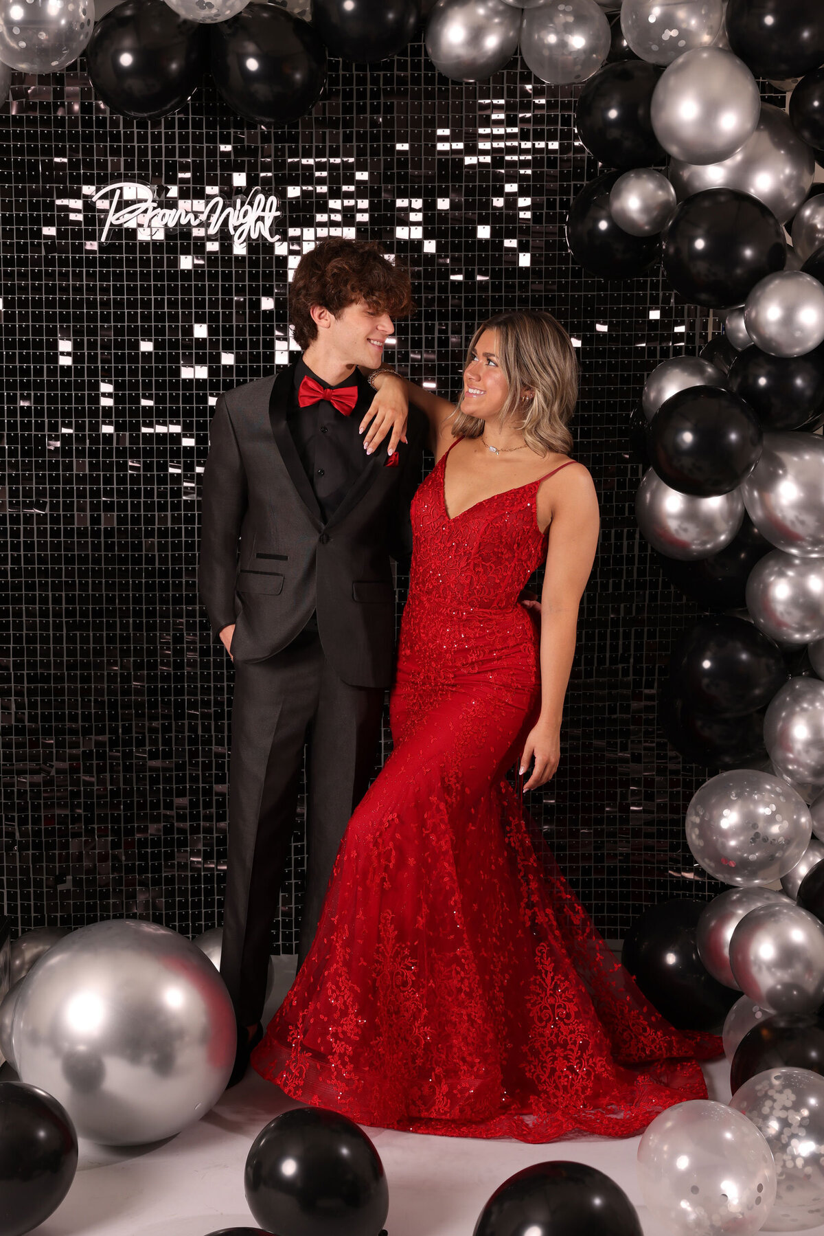 A girl wearing a dress and a boy wearing a coordinating high school prom suit while standing with balloons