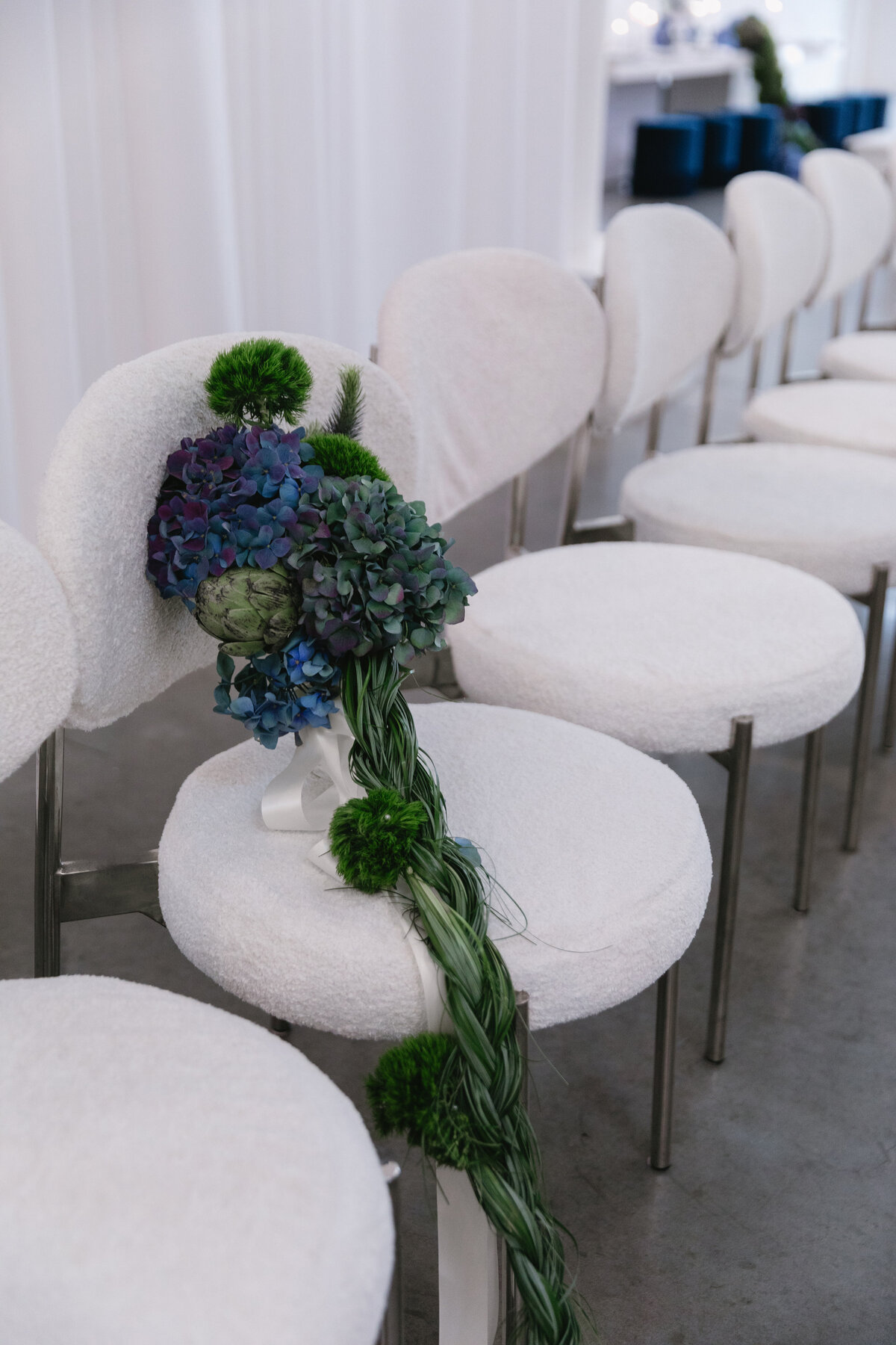 Blue and green sculptural bouquet resting on a soft white ceremony chair during an editorial New York City wedding photoshoot.