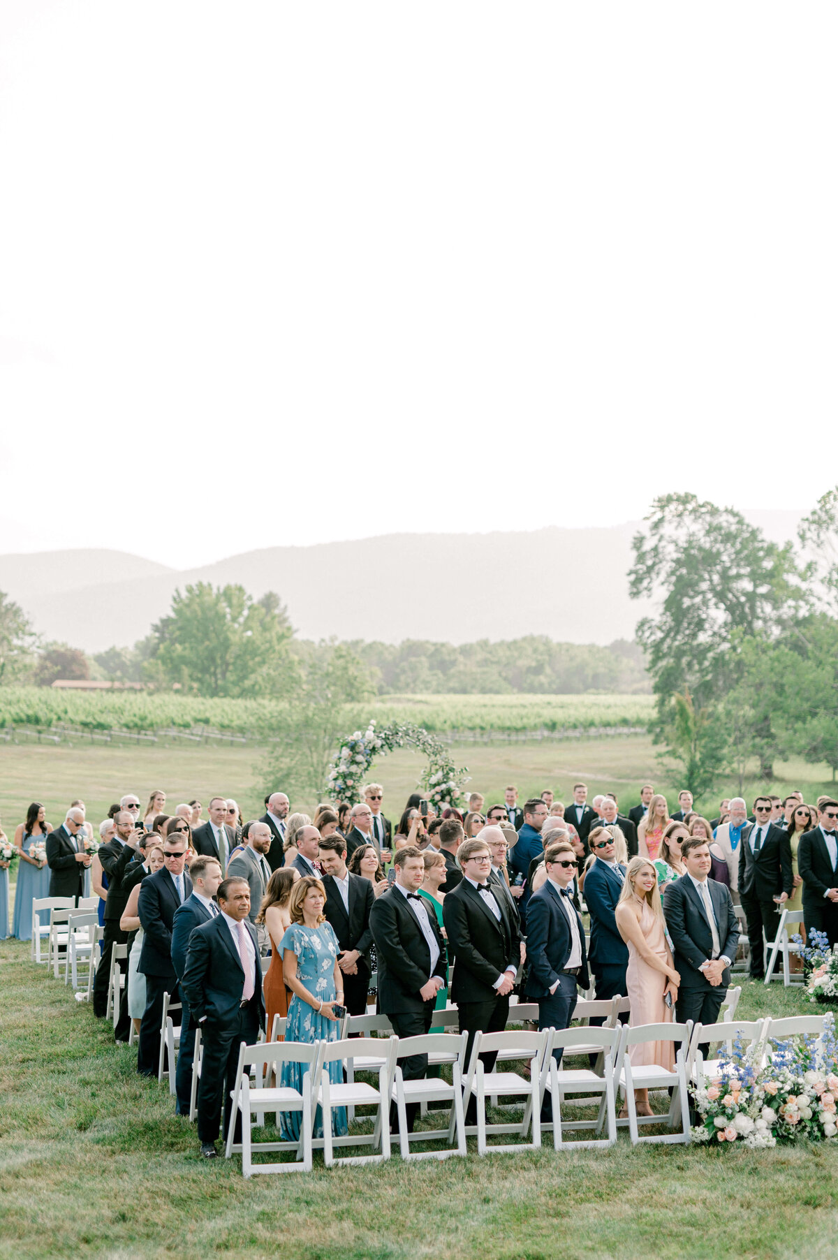 Guests watching joyfully as bride walks down the aisle with mountains in the background