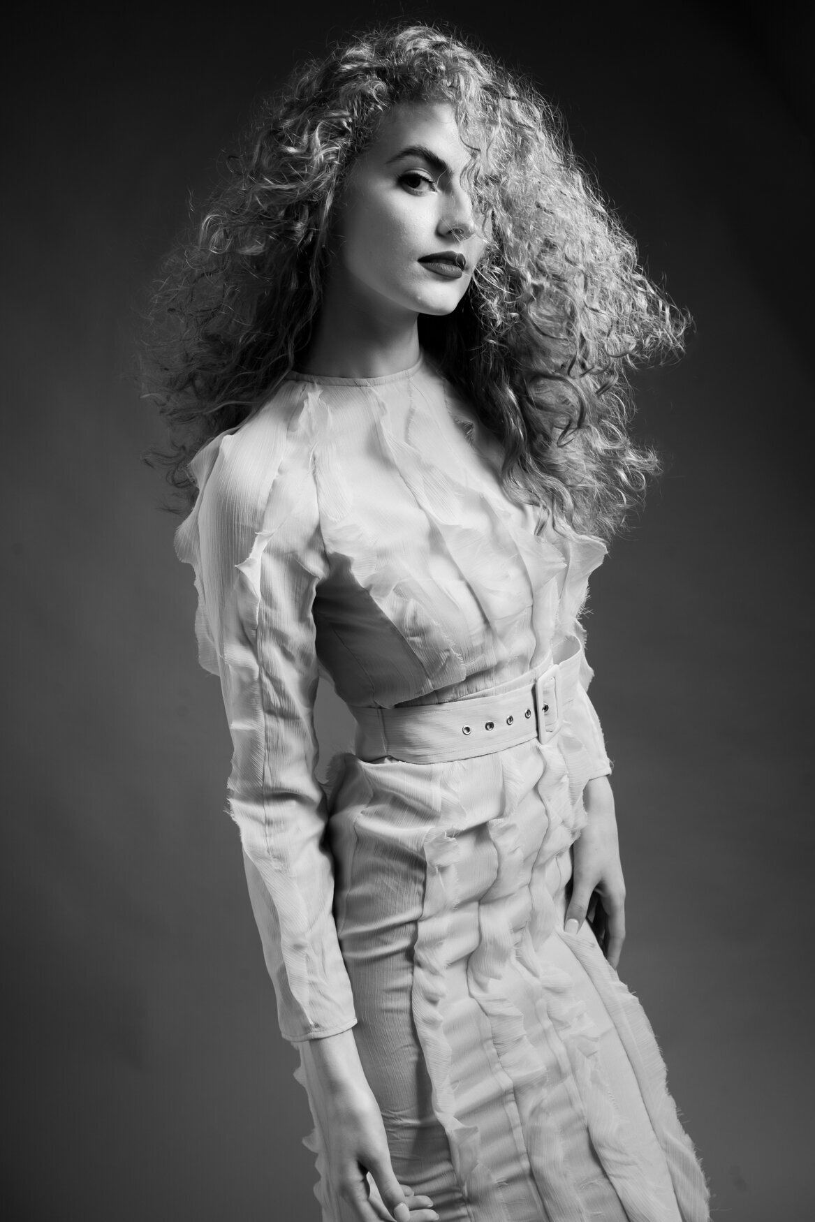 A woman with long curly hair standing in front of the amera with a side of her face covered by her hair