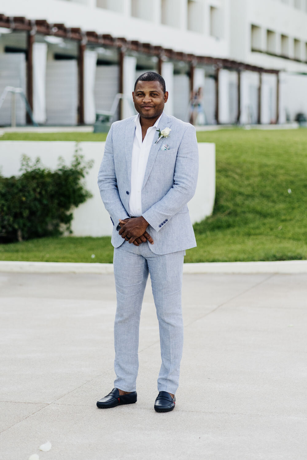 Groom standing outdoors in a light grey suit, smiling