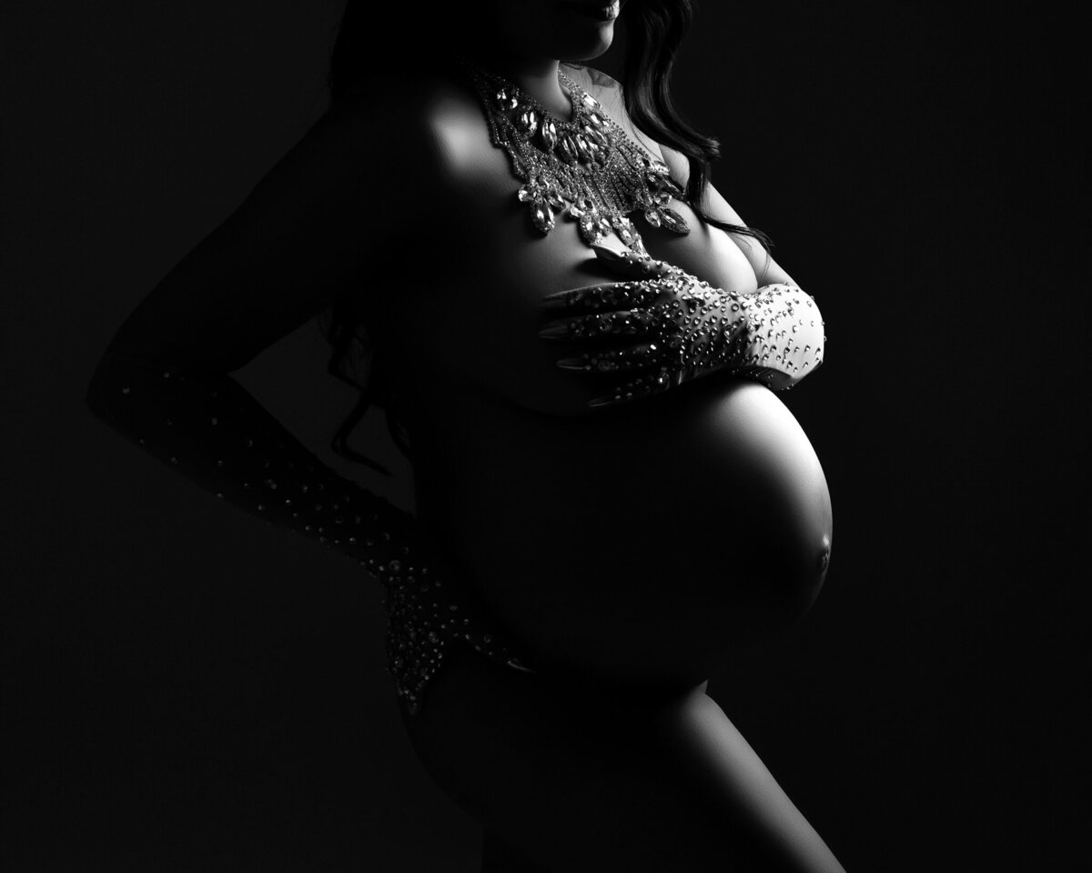 Striking black and white maternity photo with crystal gloves and statement jewelry, highlighting the baby bump in dramatic studio lighting.