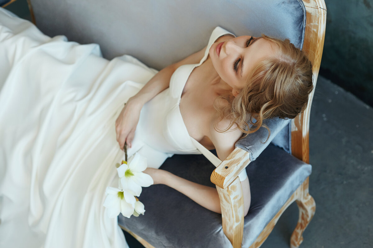 beautiful-slender-blonde-girl-sitting-sofa-long-white-dress