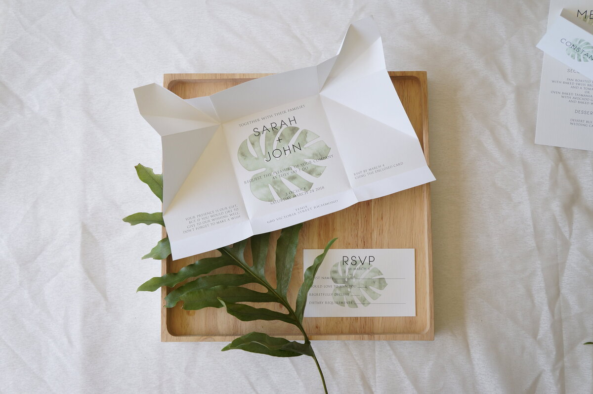 Unfolded origami wedding invitation with tropical green leaf and matching RSVP card