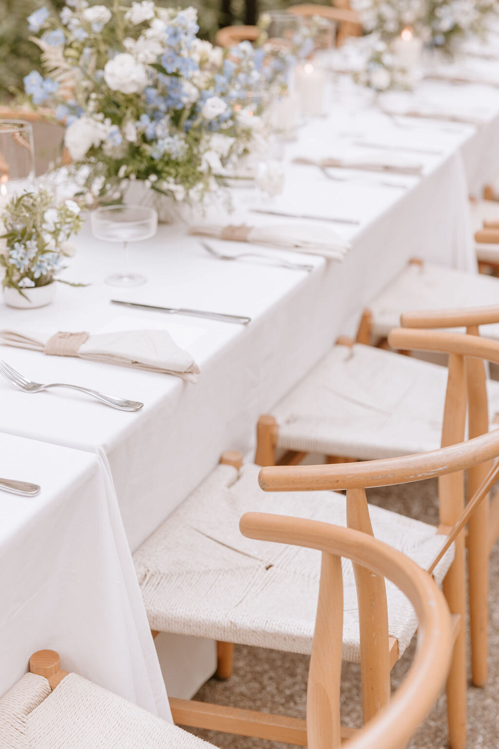 Close up of wishbone chairs and long rectangle reception table with blue and white flowers on top