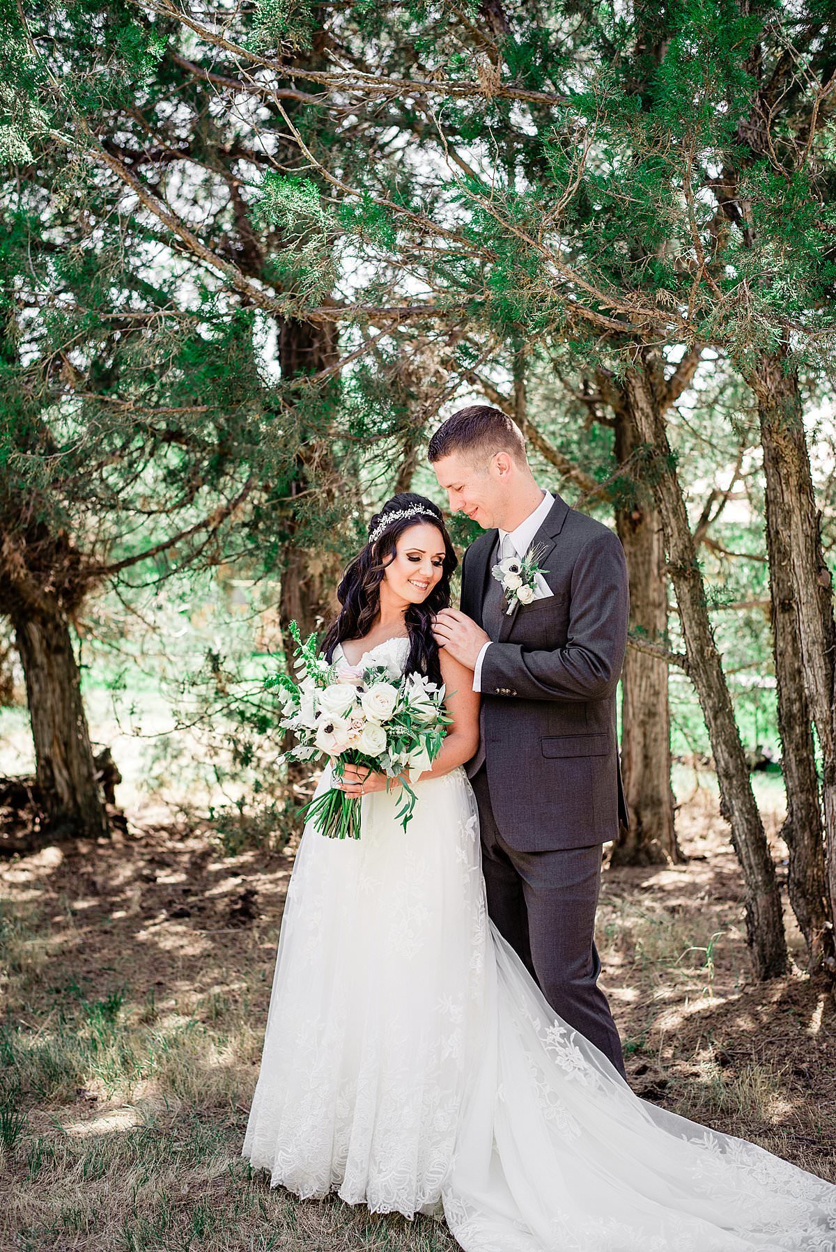 Bride smiling with her husband on their wedding day standing amongst the evergreen trees in the  shade