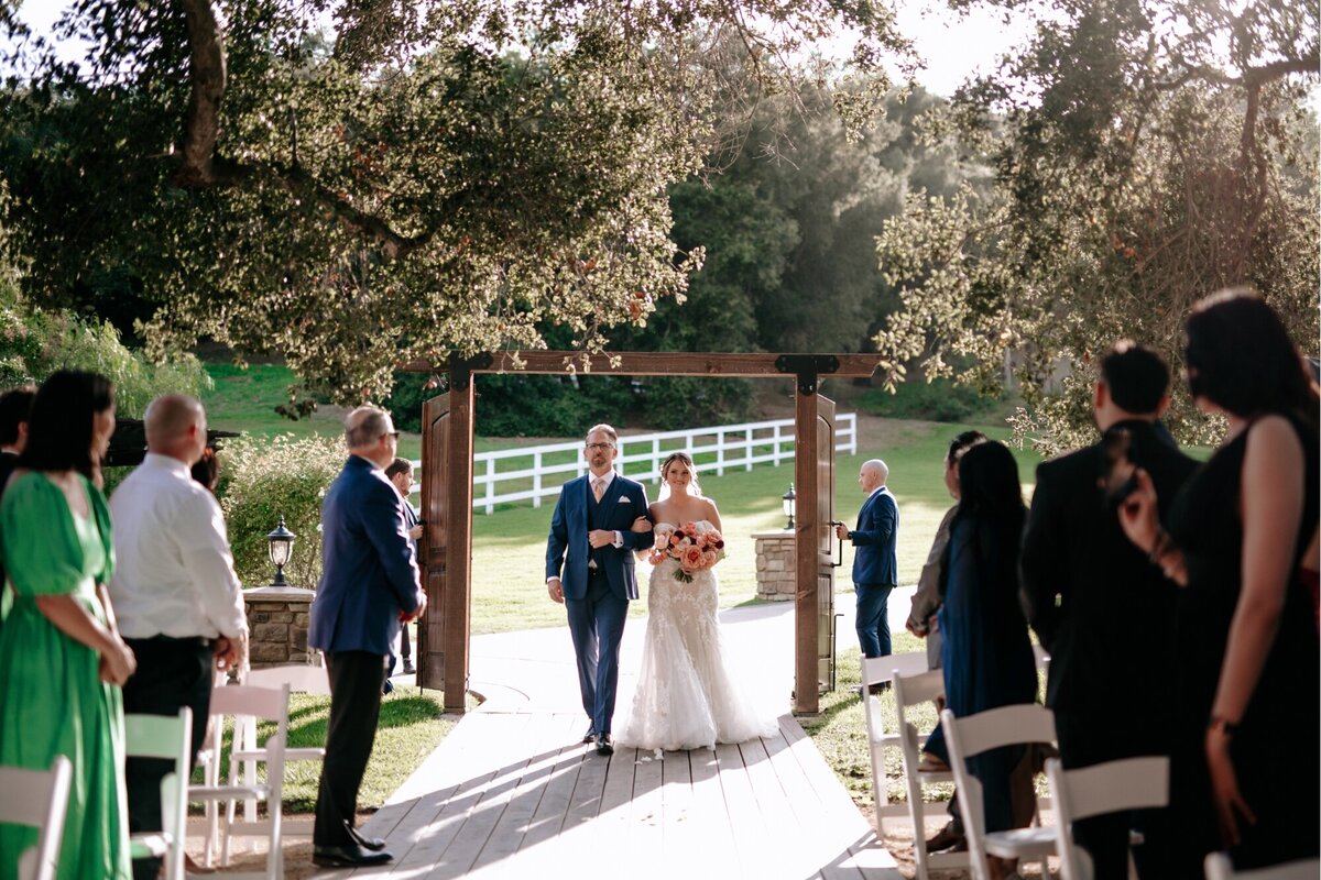 Bride and her Father walking down the aisle while her guests are standing and watching her.