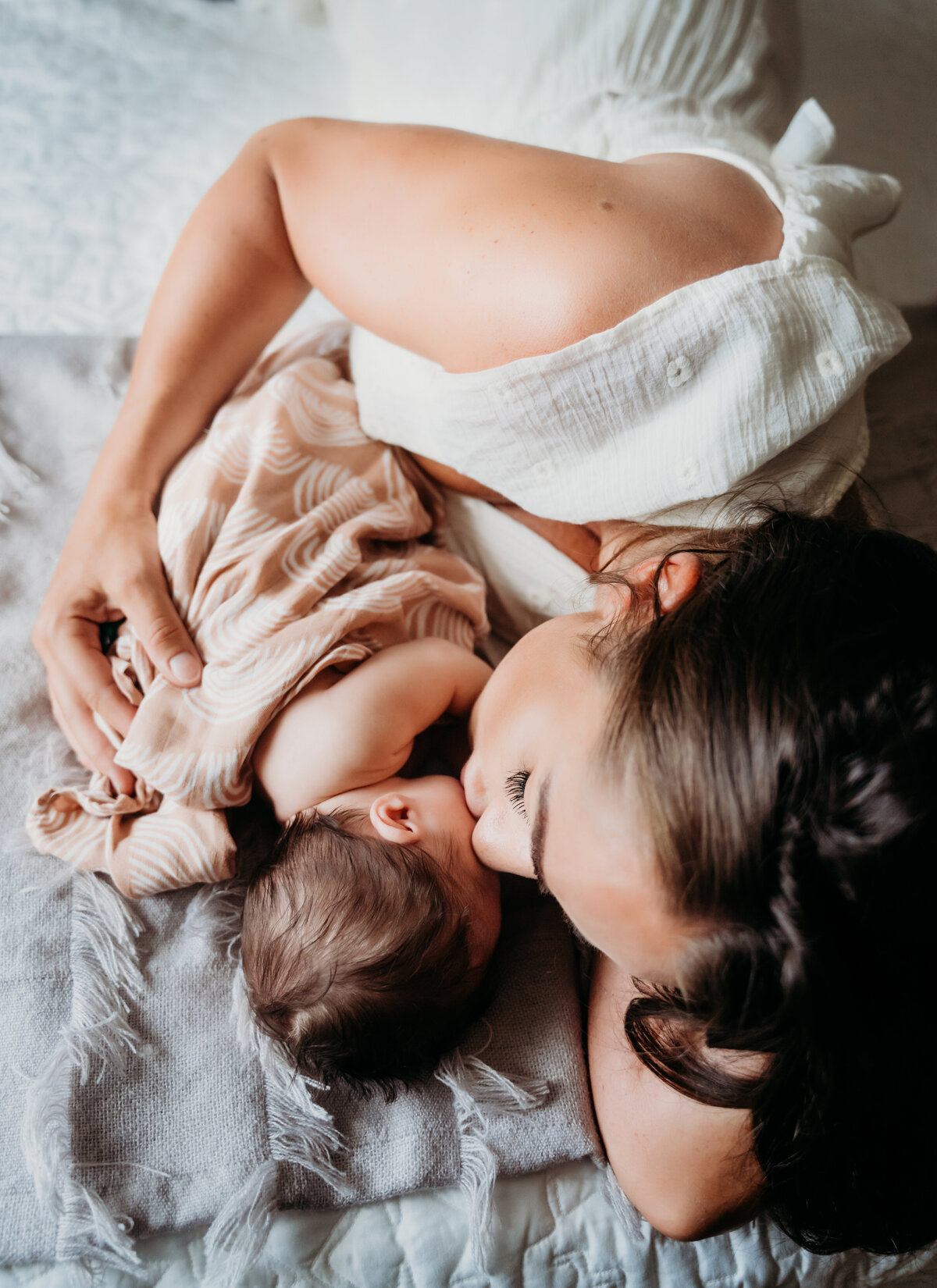 Newborn Photographer, a mother lays on her bed and kisses baby beside her