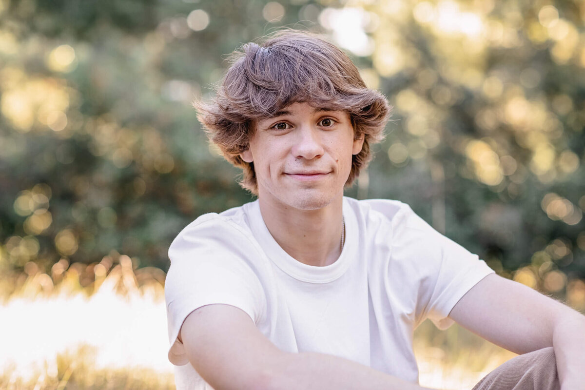 A close-up of a young man with brown hair wearing a white shirt surrounded by greenery at Jeffrey Open Space in Irvine.