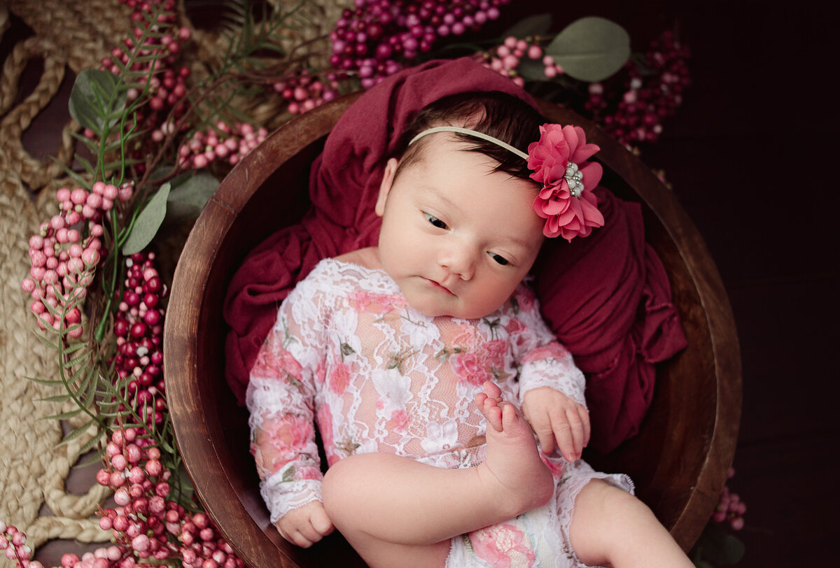 Baby girl wearing lace romper laying in wood bowl during newborn photoshoot in Mount Juliet tennessee photography studio