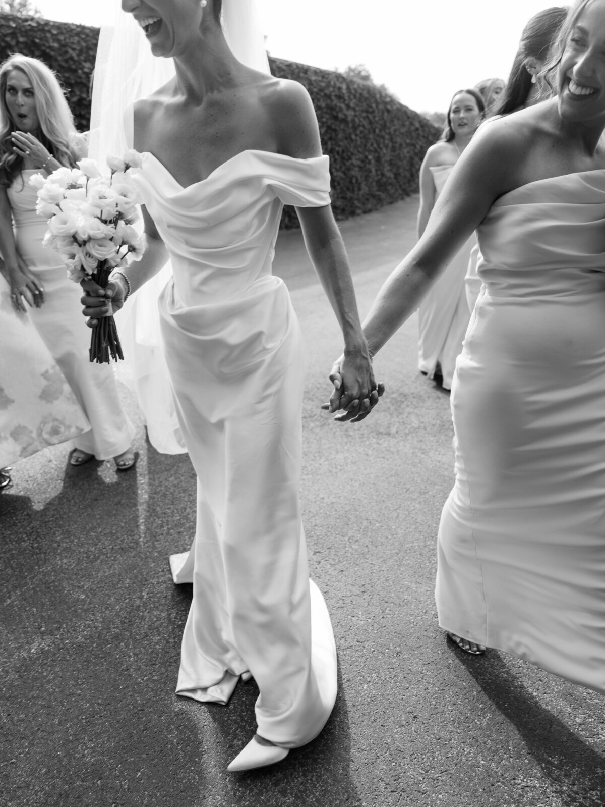 black and white image of bride holding hands with her maid of honor walking and laughing taken by Mansfield Wedding Photographer, Annie Trammel
